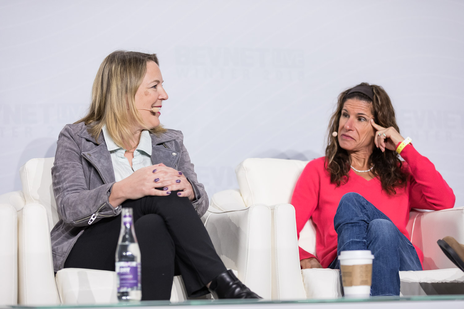 Two women in armchairs on stage, one in a light jacket, one in a red top.
