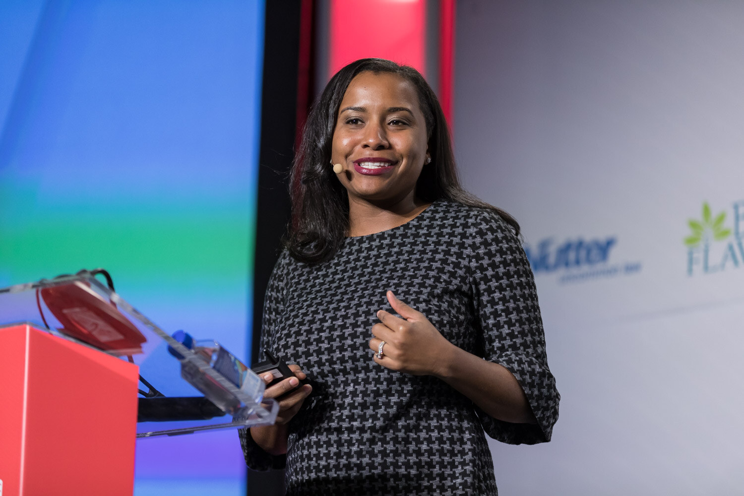 Woman in a houndstooth dress smiling at a podium on stage.