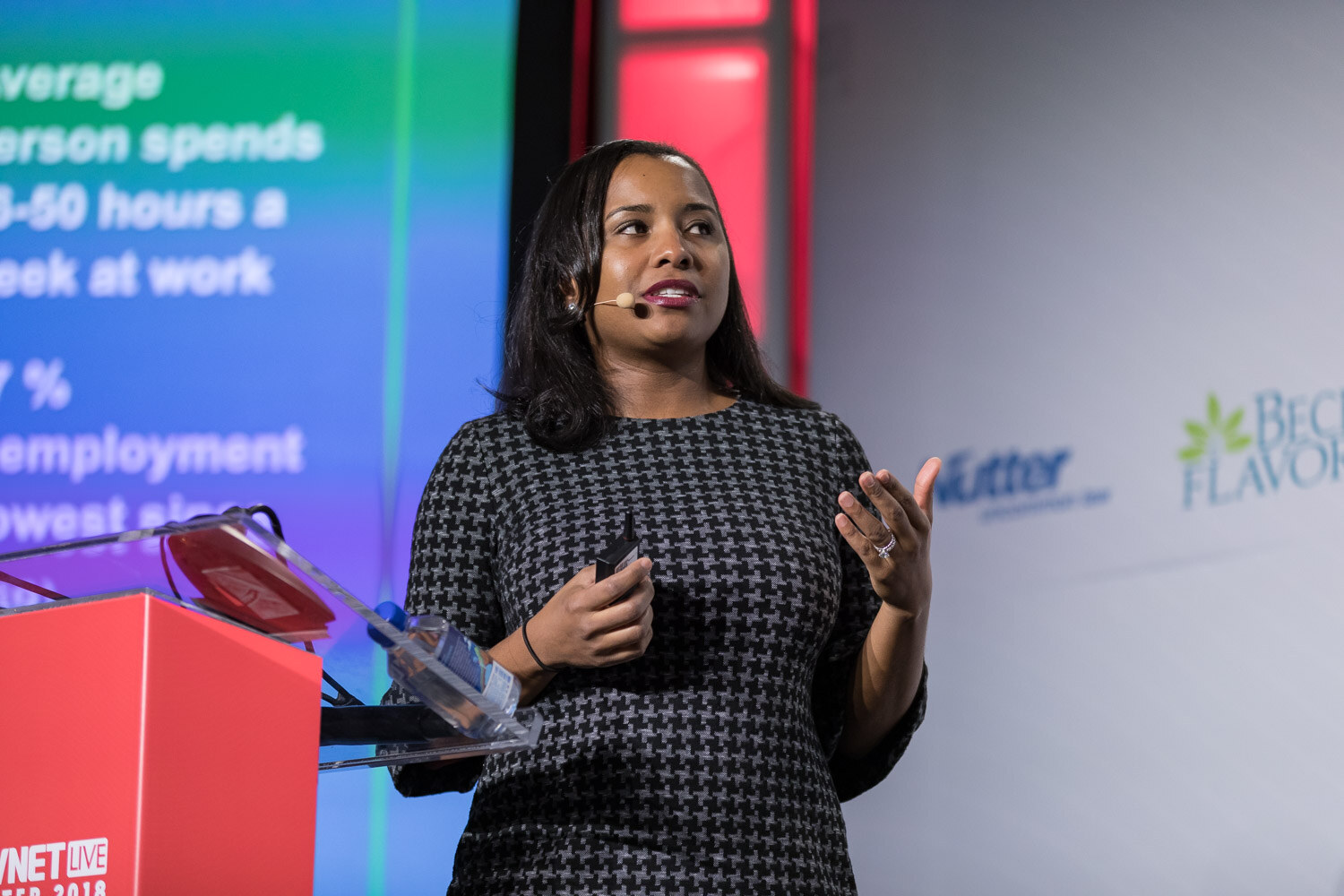Woman in a patterned dress at a podium next to a green and blue slide with statistics.