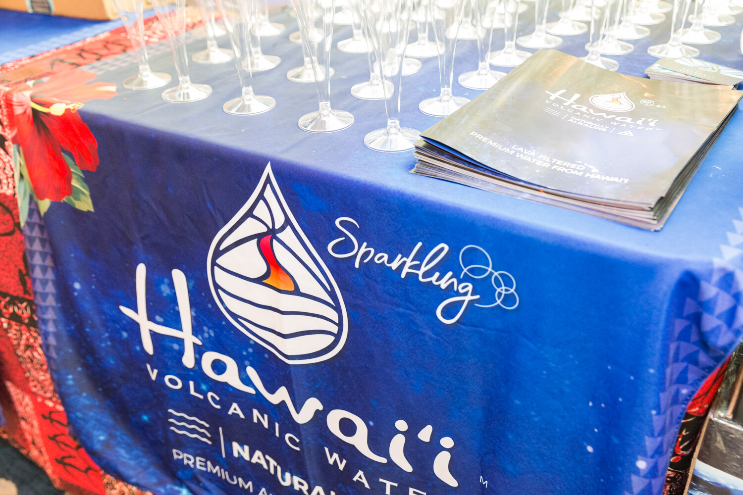 Blue tablecloth with a Hawaii sparkling water logo and a tray of glasses.