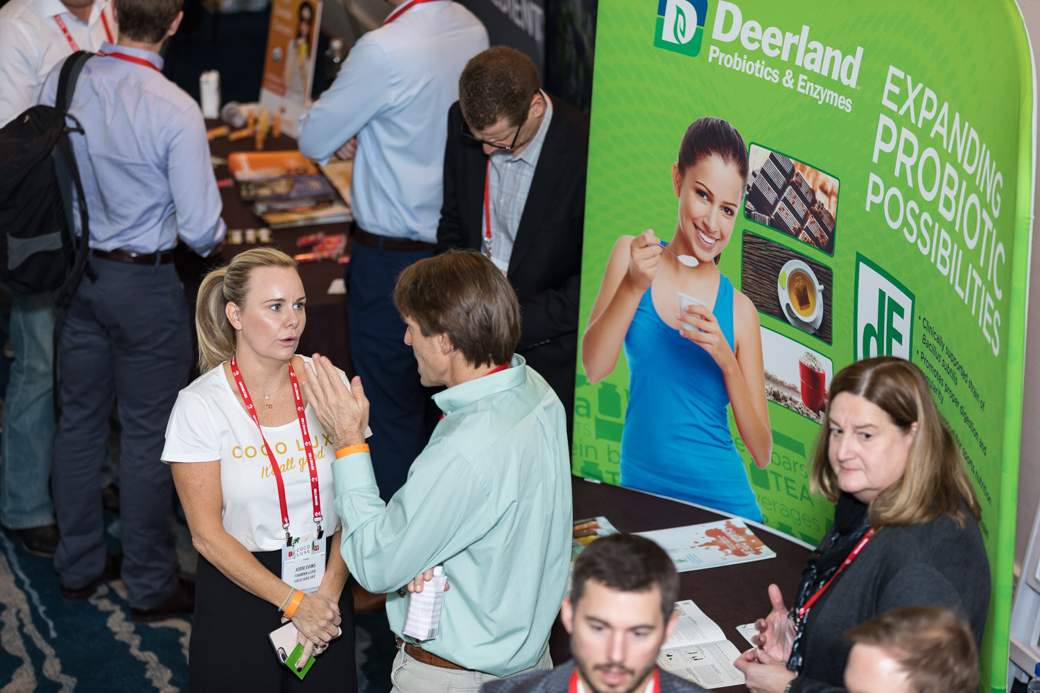 High angle view of attendees talking in front of a Deerland Probiotics banner.