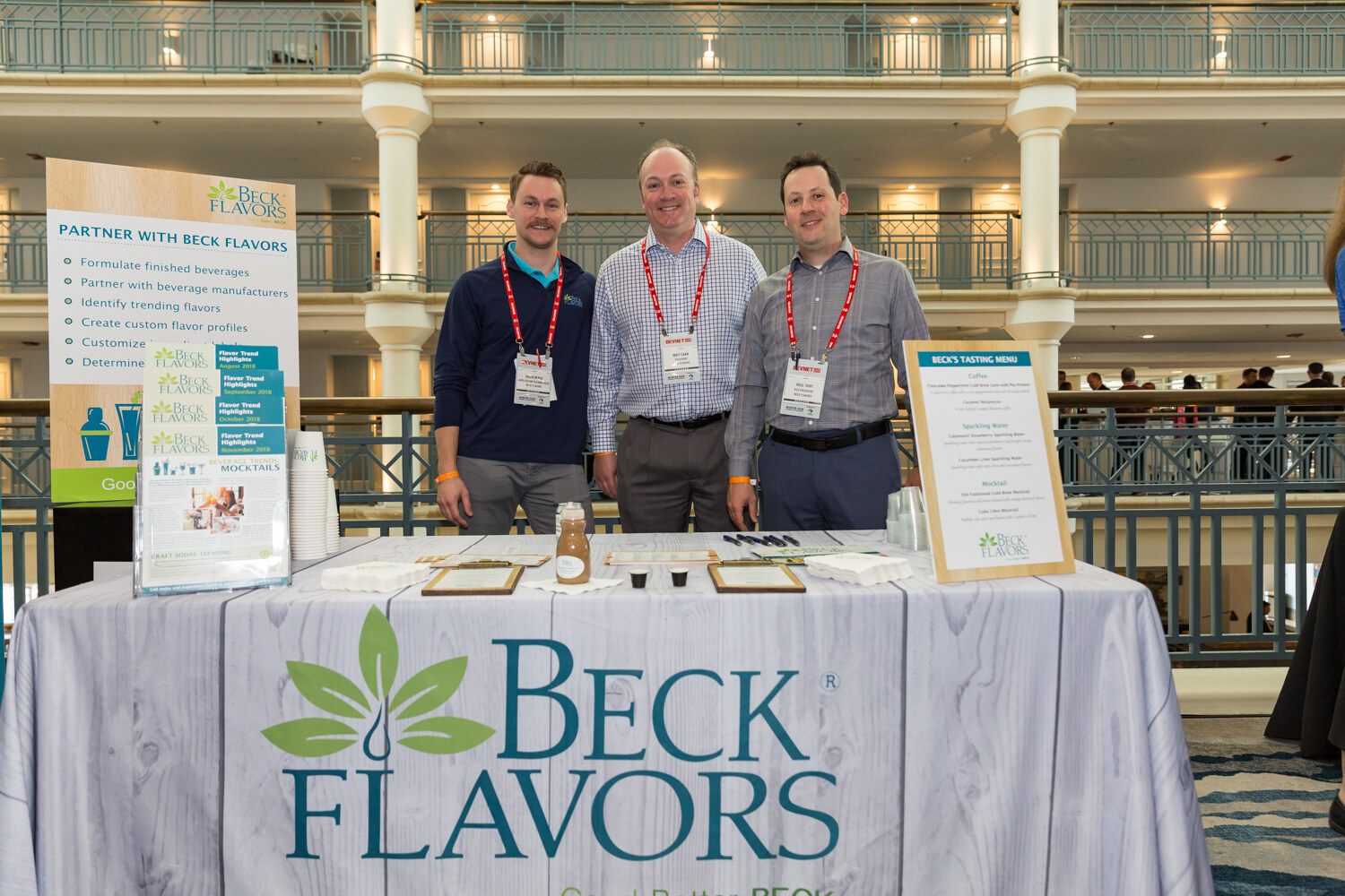 Three men behind a table with a Beck Flavors tablecloth.