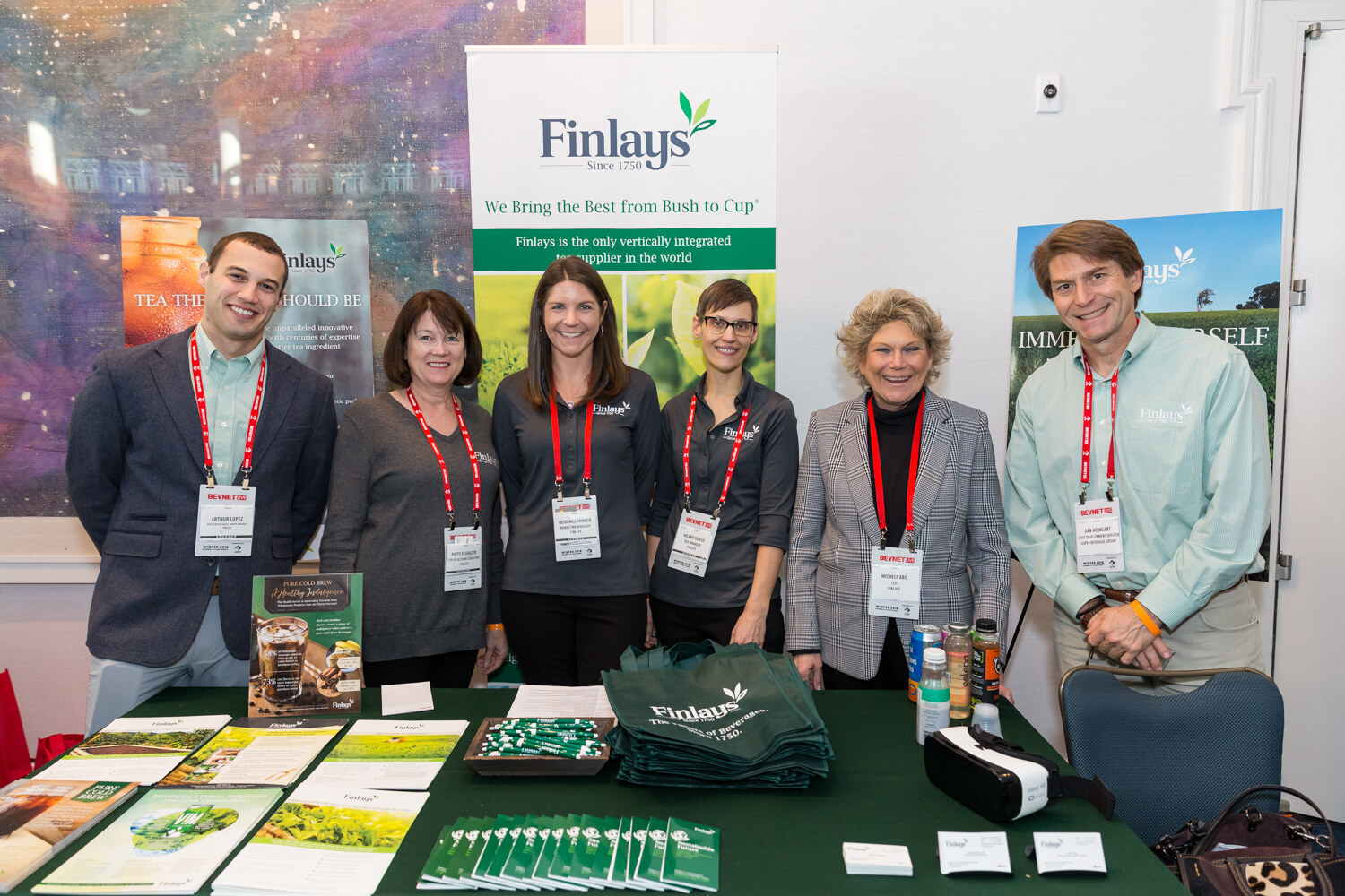Group of six people in front of a Finlays banner and a table with tea samples.