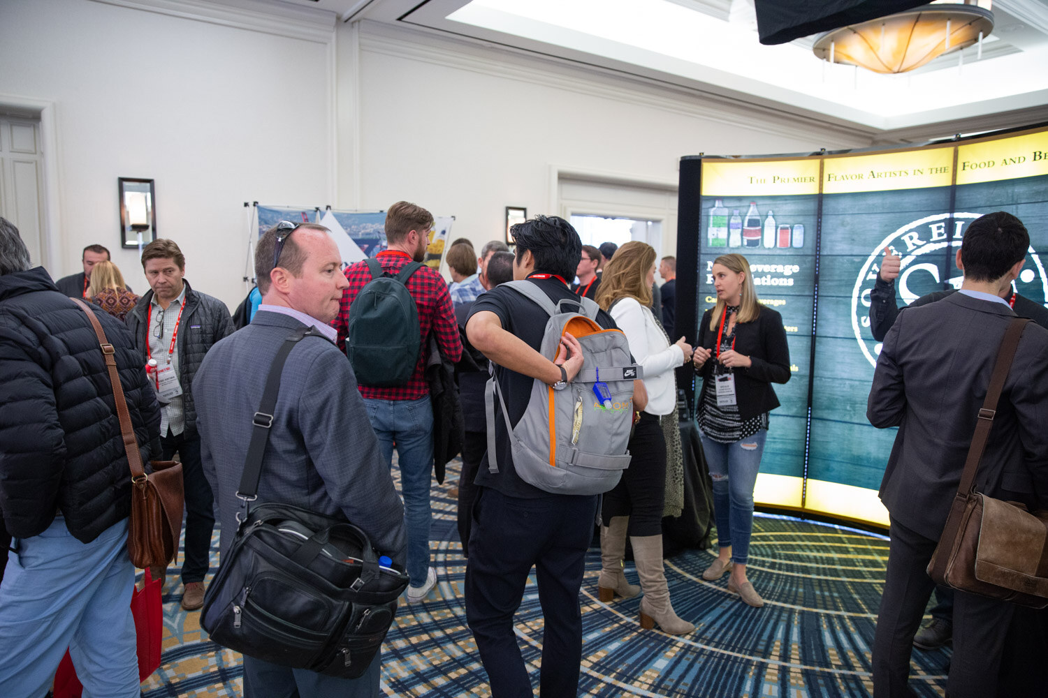 Crowded hotel ballroom with attendees walking past exhibit displays.