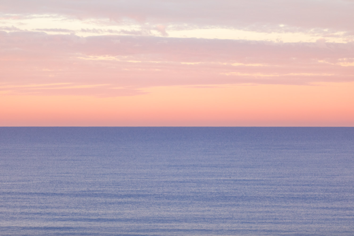 Pink and orange sunrise sky over a calm ocean horizon.