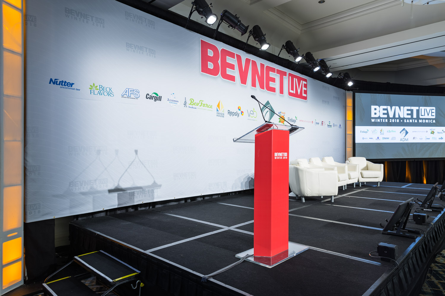 Empty stage with a red podium, white chairs and a BevNET Live sponsor backdrop.