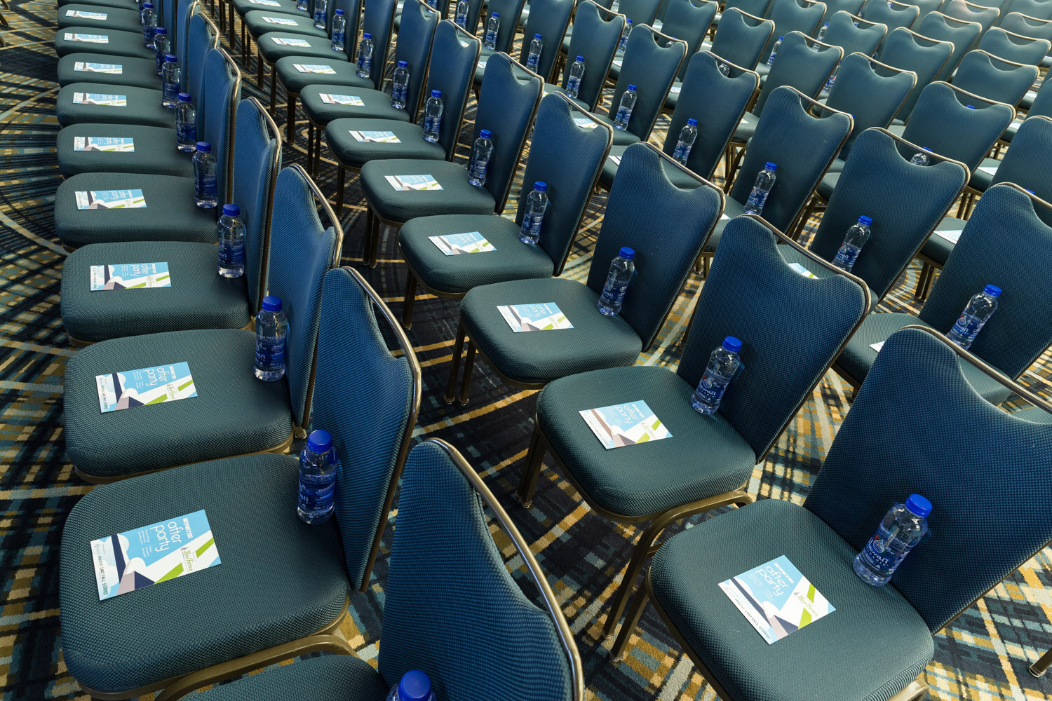 Close view of teal ballroom chairs with printed cards and small water bottles on the seats.