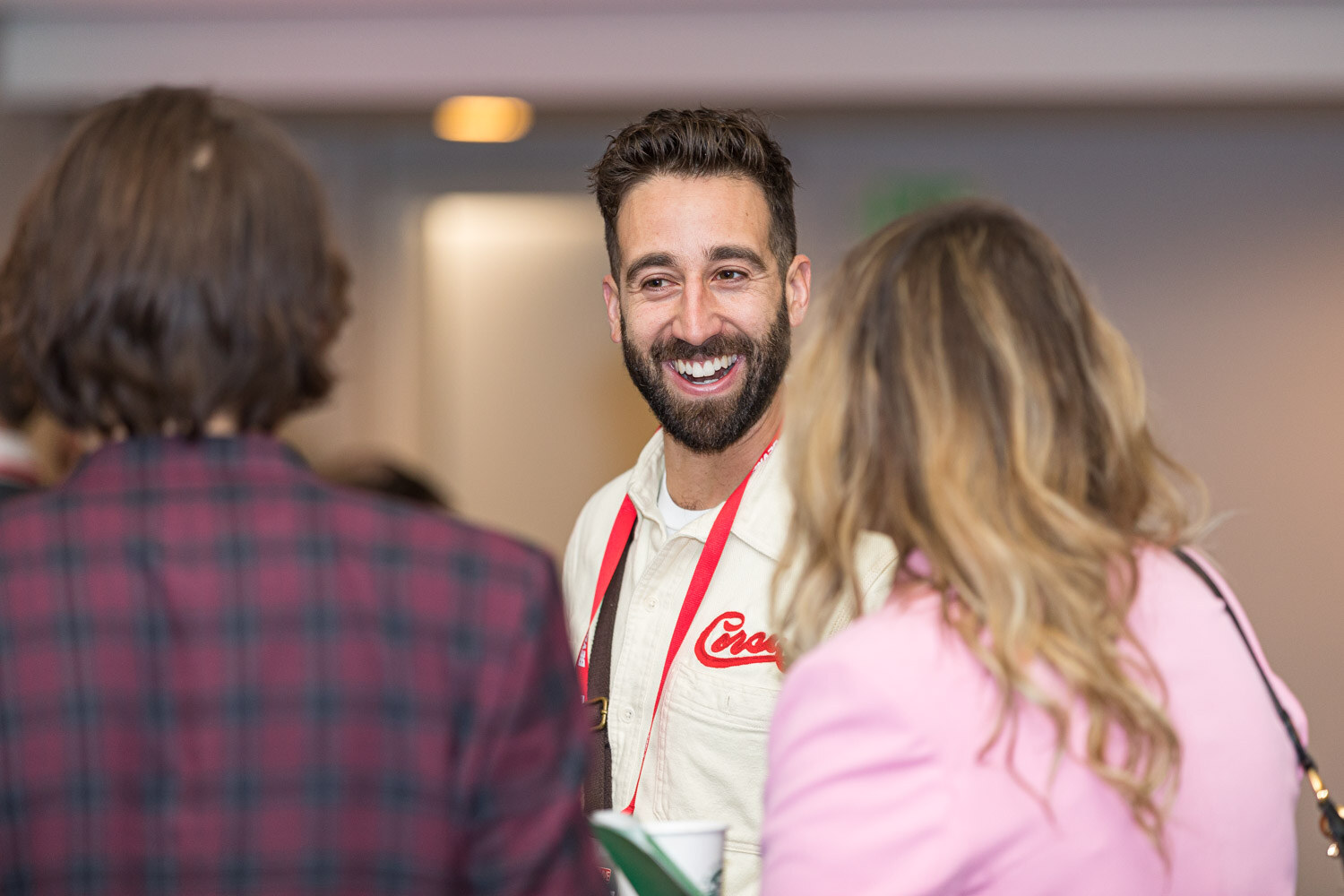 A smiling bearded man wearing a Corsa shirt talks with a woman in a pink jacket and another attendee.