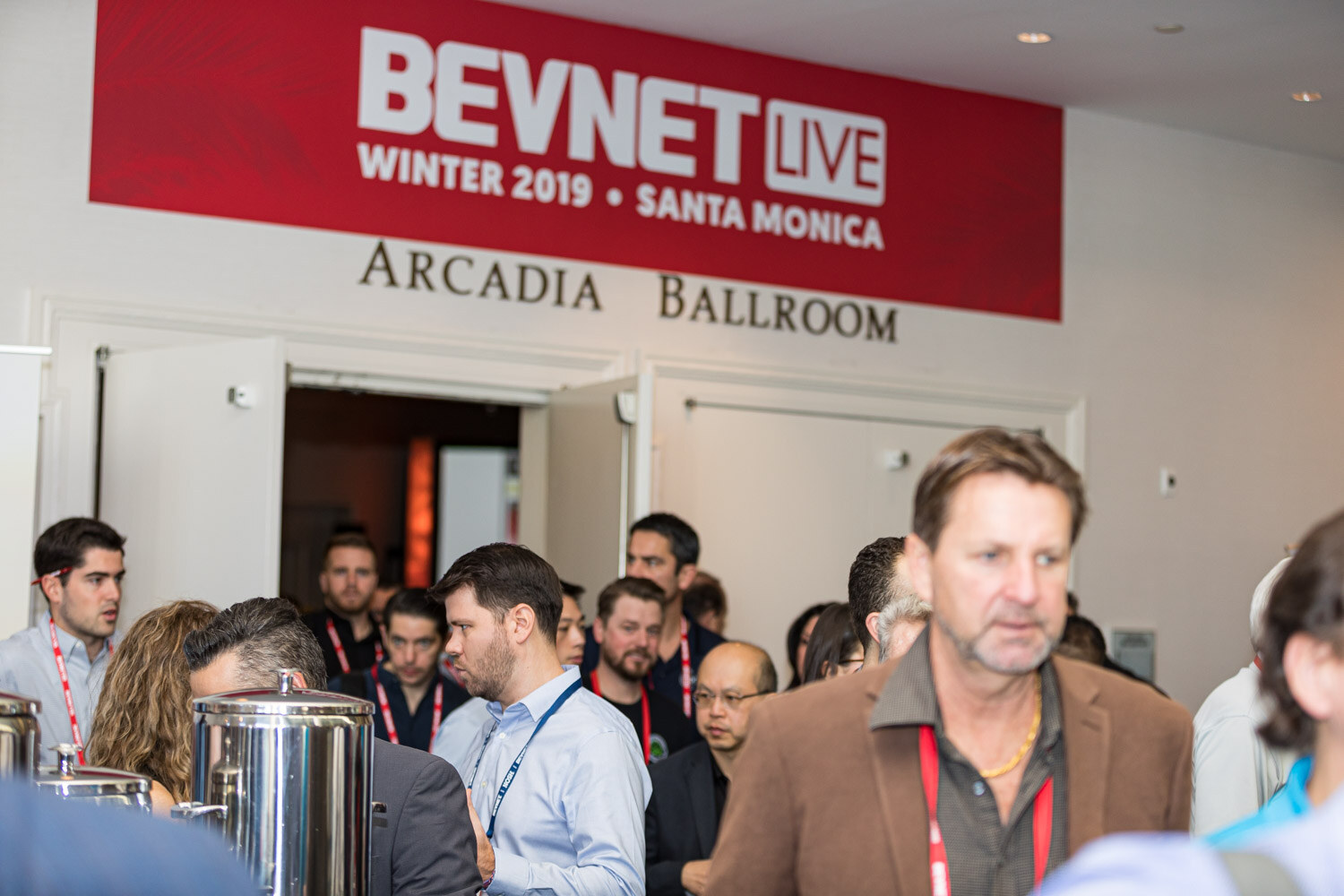 A crowd of attendees stands beneath a BevNET Live Winter 2019 Santa Monica Arcadia Ballroom sign next to coffee urns.