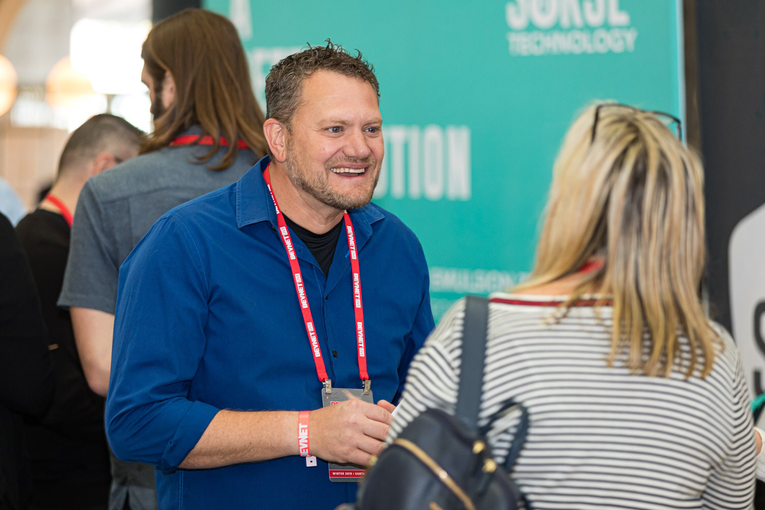A smiling man with a red lanyard talks with a woman in a striped top in front of a teal Sorse Technology banner.