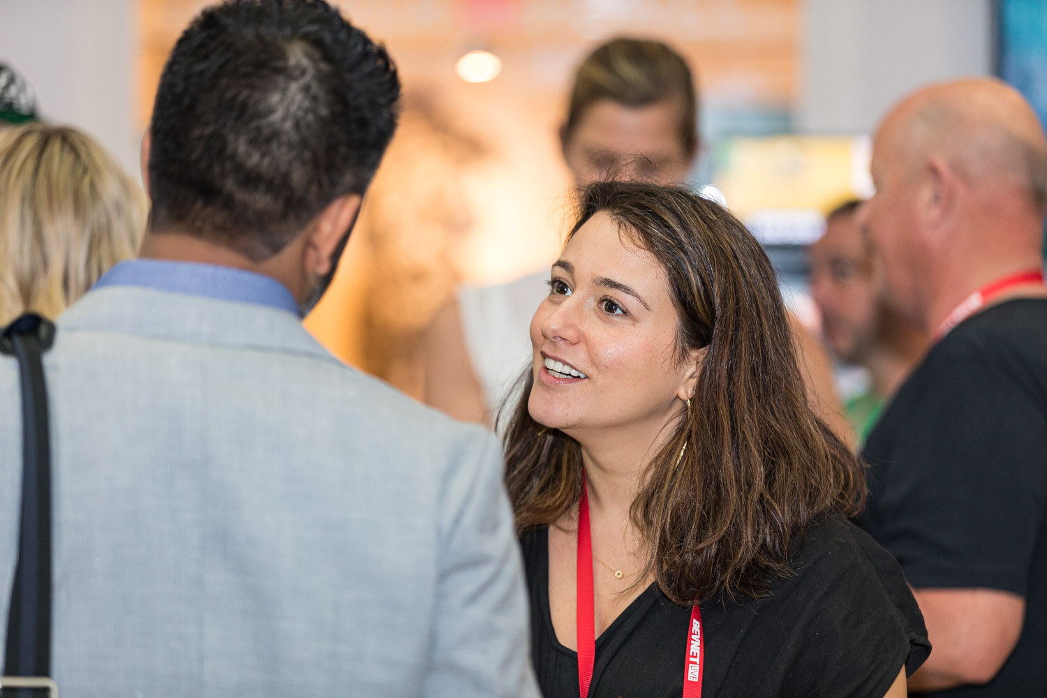A woman with long dark hair smiles and talks with a man whose back is turned to the camera.