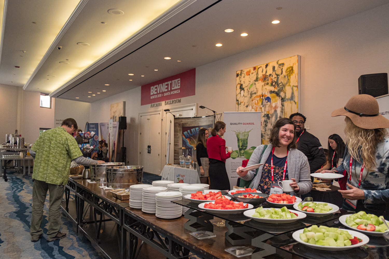 Attendees serve themselves fruit from a long buffet table in a ballroom foyer with BevNET Live signage.