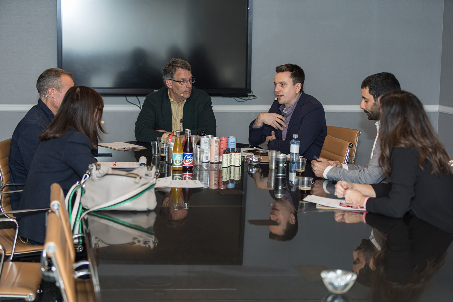 Several people sit around a dark conference table covered with cans, bottles and notes in a hotel meeting room.