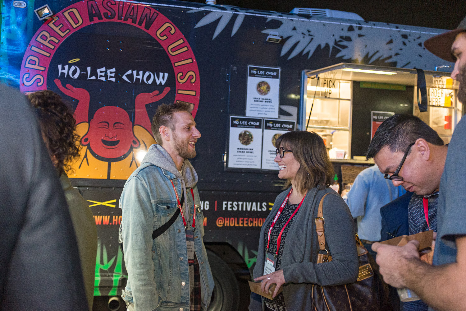 Attendees stand at a Ho-Lee Chow food truck with colorful signage at night.