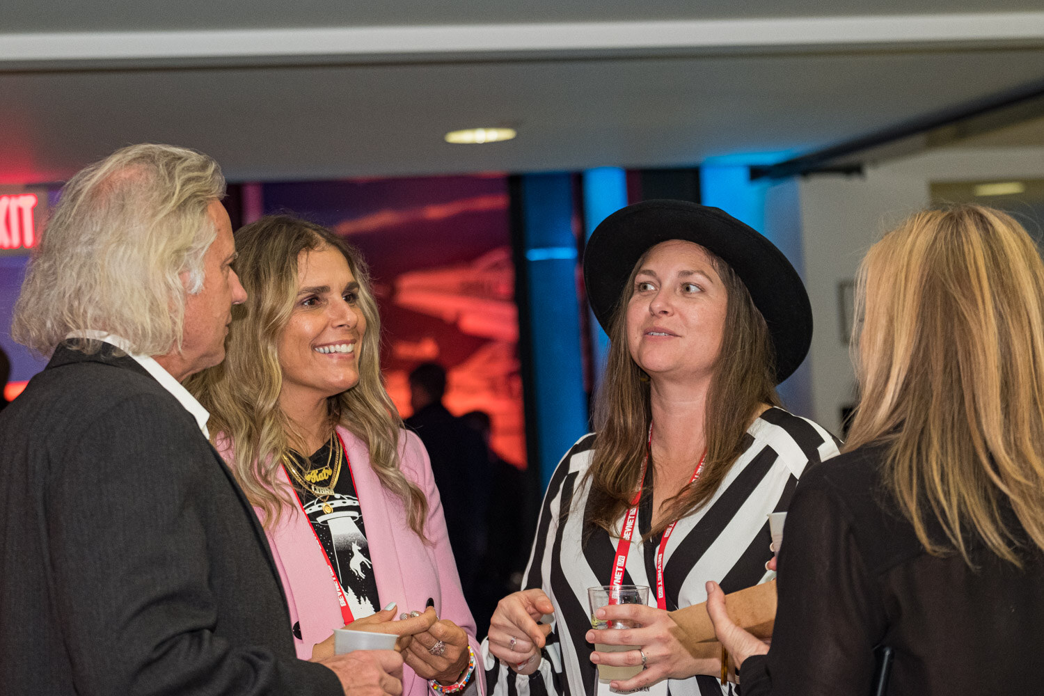 Four people in conversation, including a woman in a black hat and one in a striped dress, inside the museum.