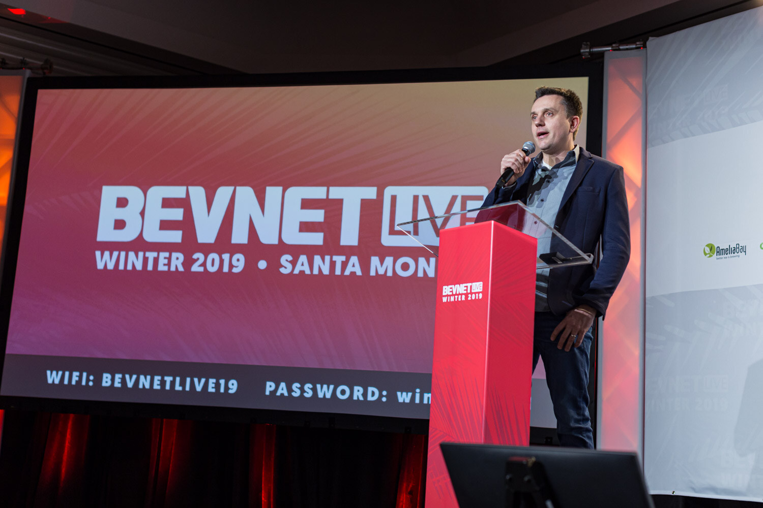 A man in a navy blazer stands at a red lectern in front of a screen reading BevNET Live Winter 2019 Santa Monica.