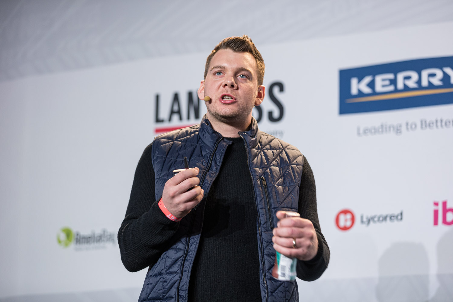 Close view of a man in a quilted vest holding a can in one hand and a pen in the other, with Lanxess and Kerry logos behind him.