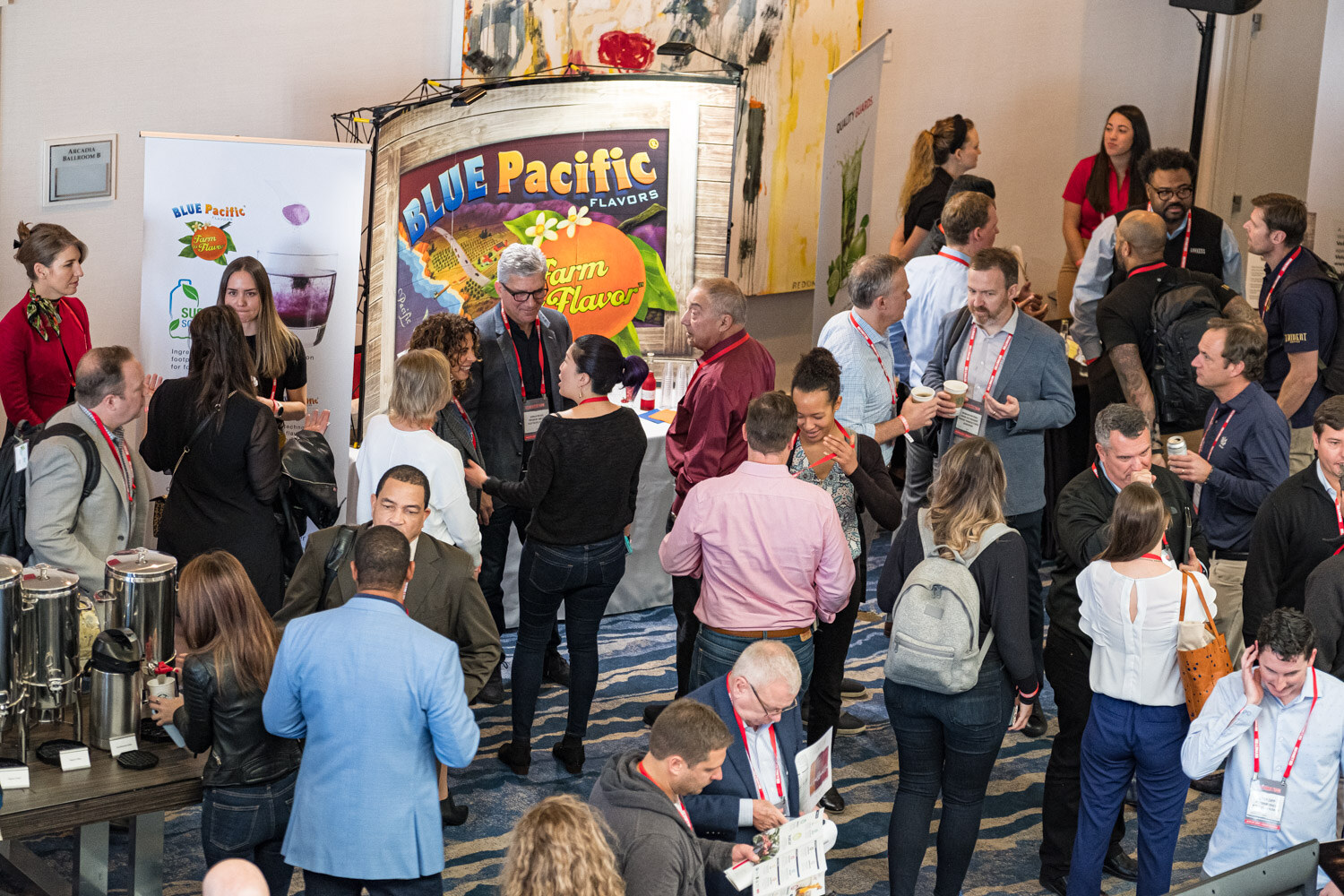 View from above of a crowd of badge-wearing attendees beside a Blue Pacific Flavors booth in the hotel atrium.