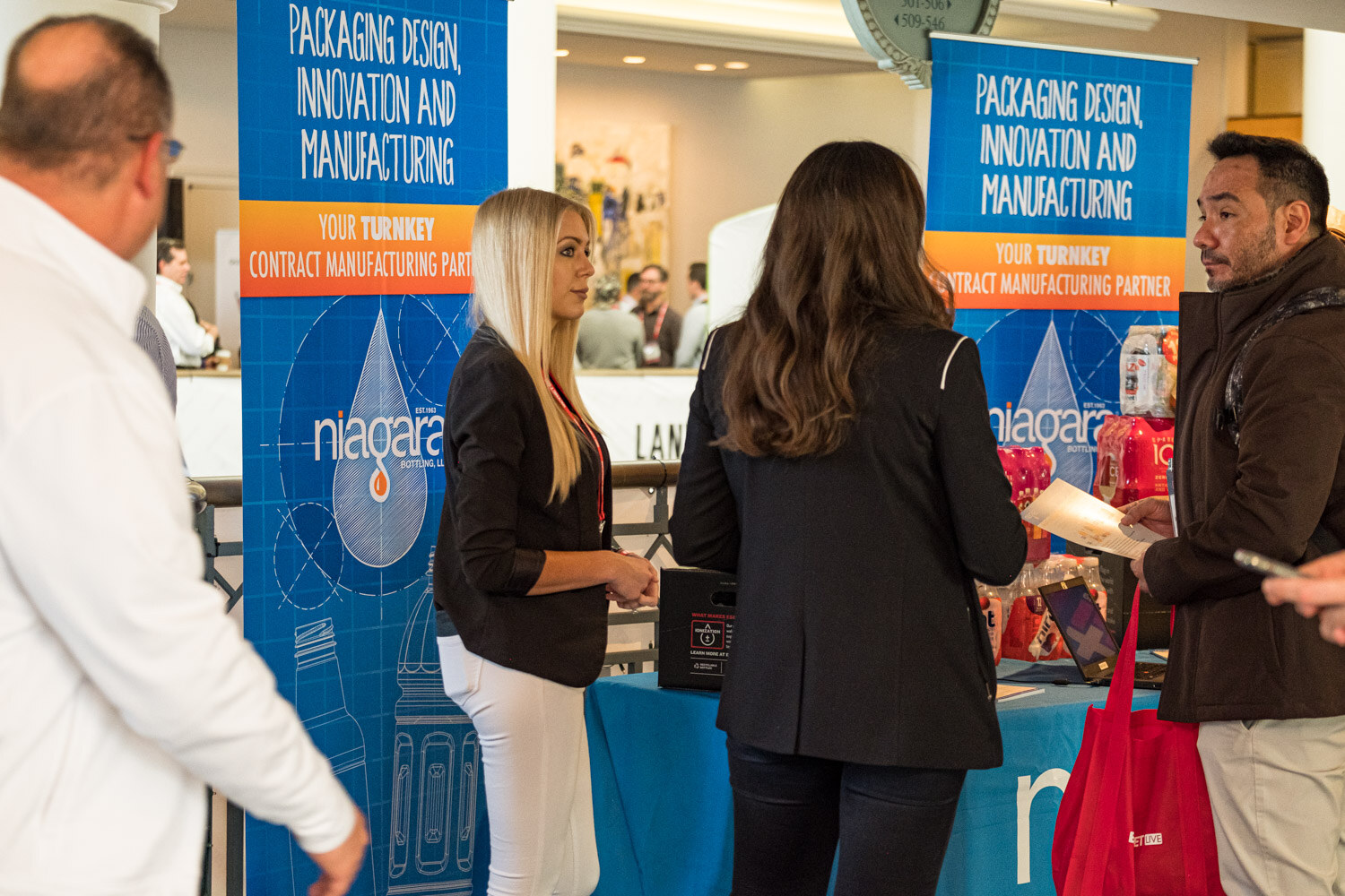 A woman in a black blazer and a woman in dark hair stand under blue Niagara banners reading Packaging design, innovation and manufacturing.