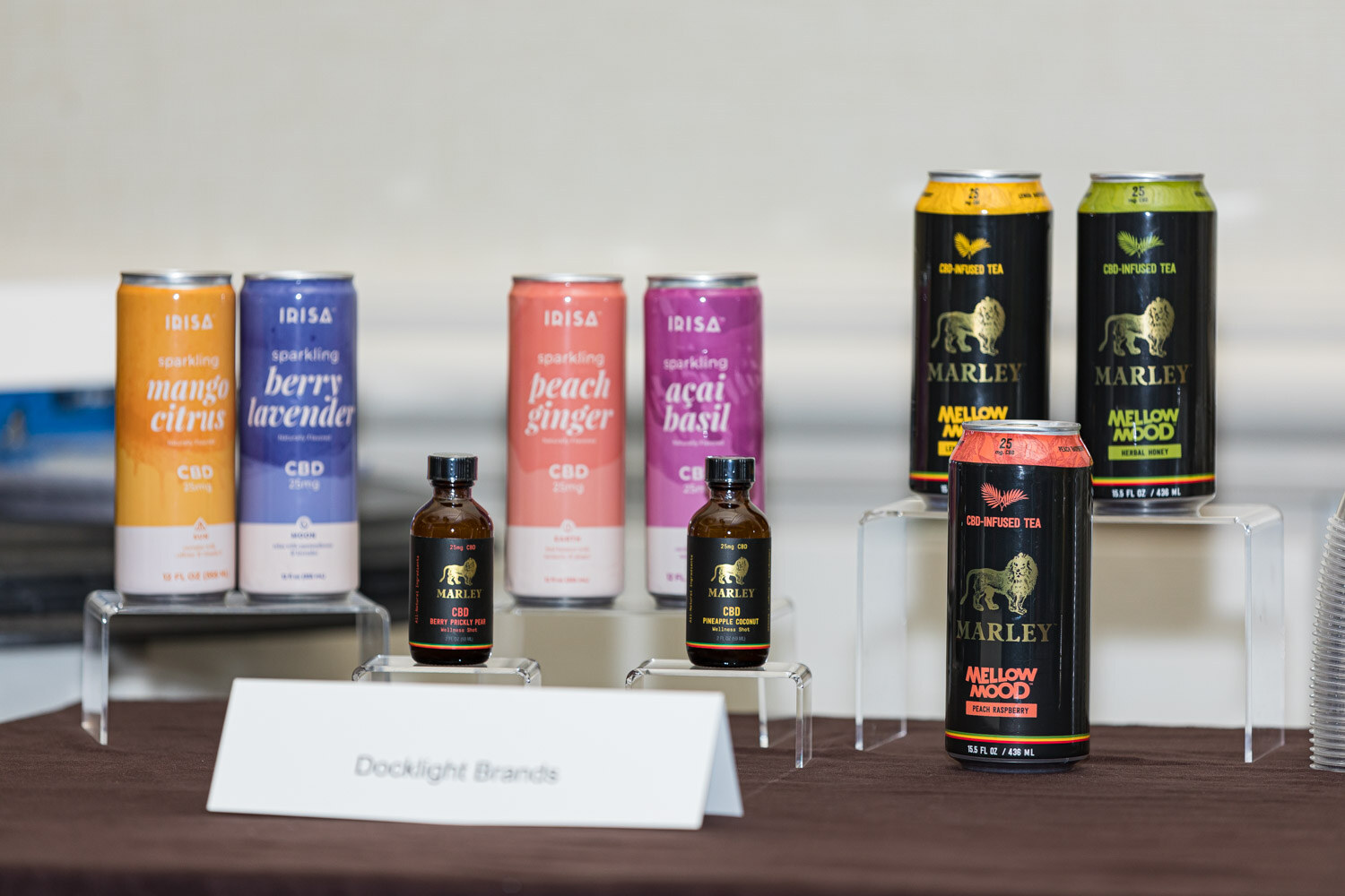 Four Irisa CBD sparkling cans and two Marley tea cans stand on risers with small tincture bottles and a Docklight Brands placard.