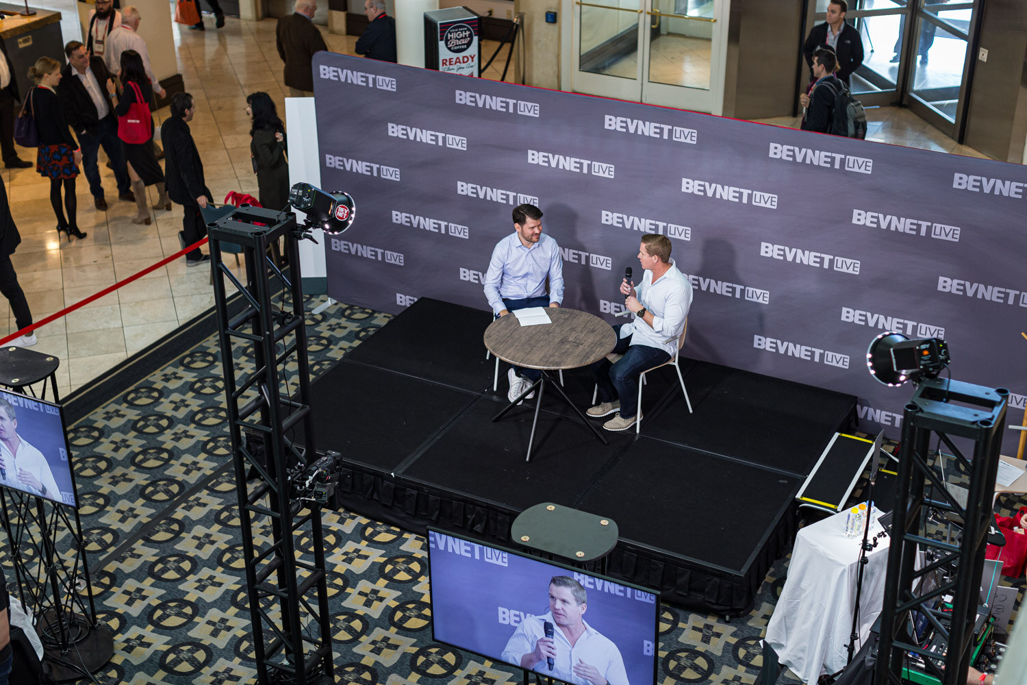 View from above of a small stage with a round table, two people being interviewed, and camera stands in the atrium.