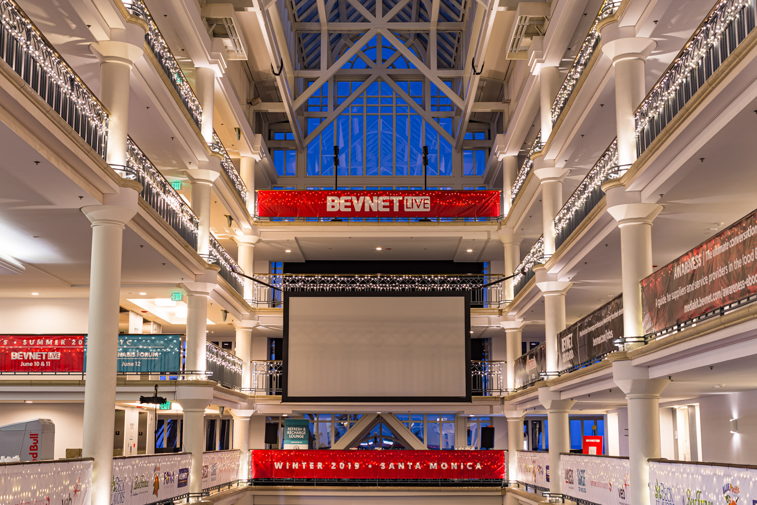 A multi-story atrium with white columns, holiday lights, a large screen and BevNET Live banners on the balconies.