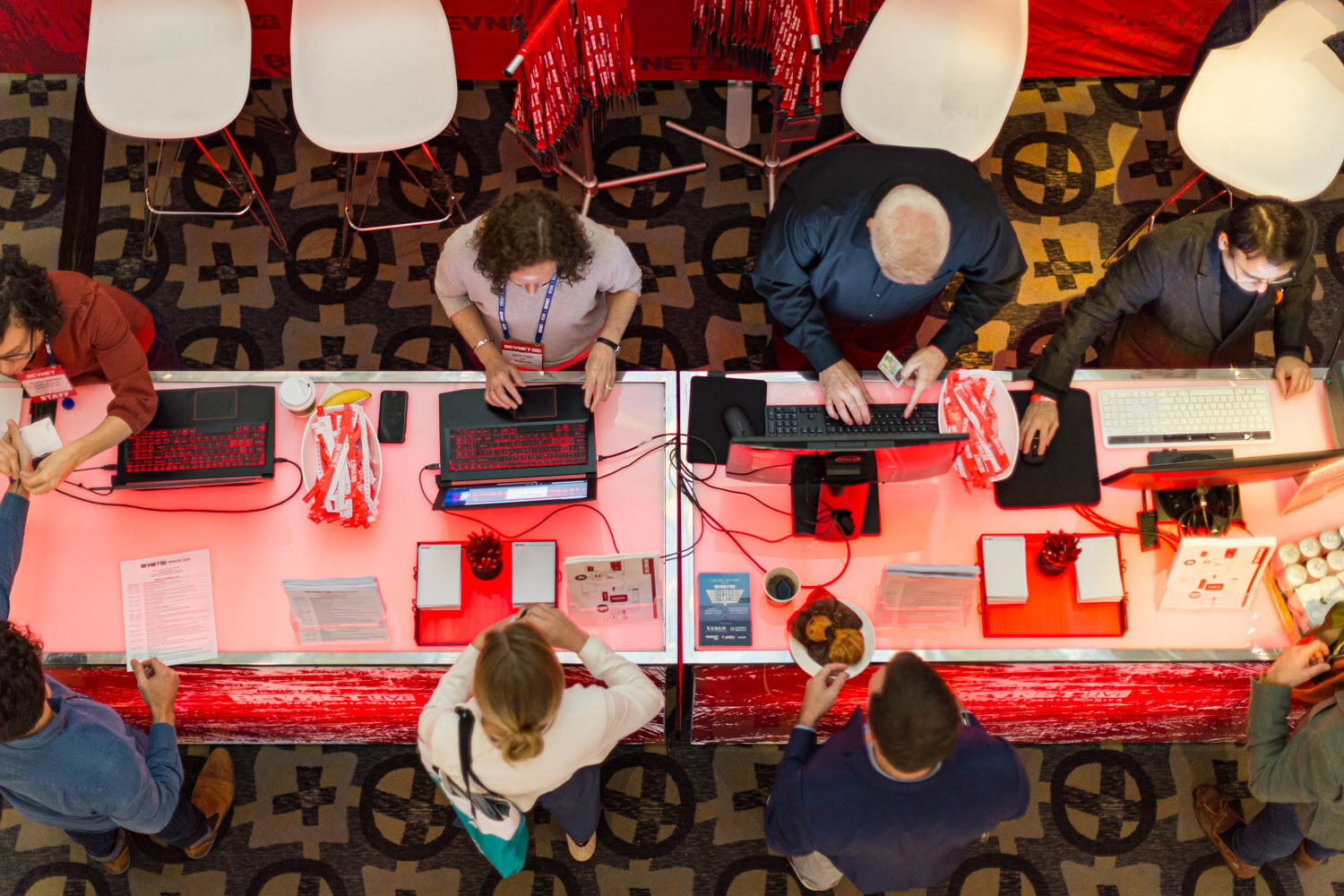 View from above of a long registration counter with laptops, staff and attendees lit in red.