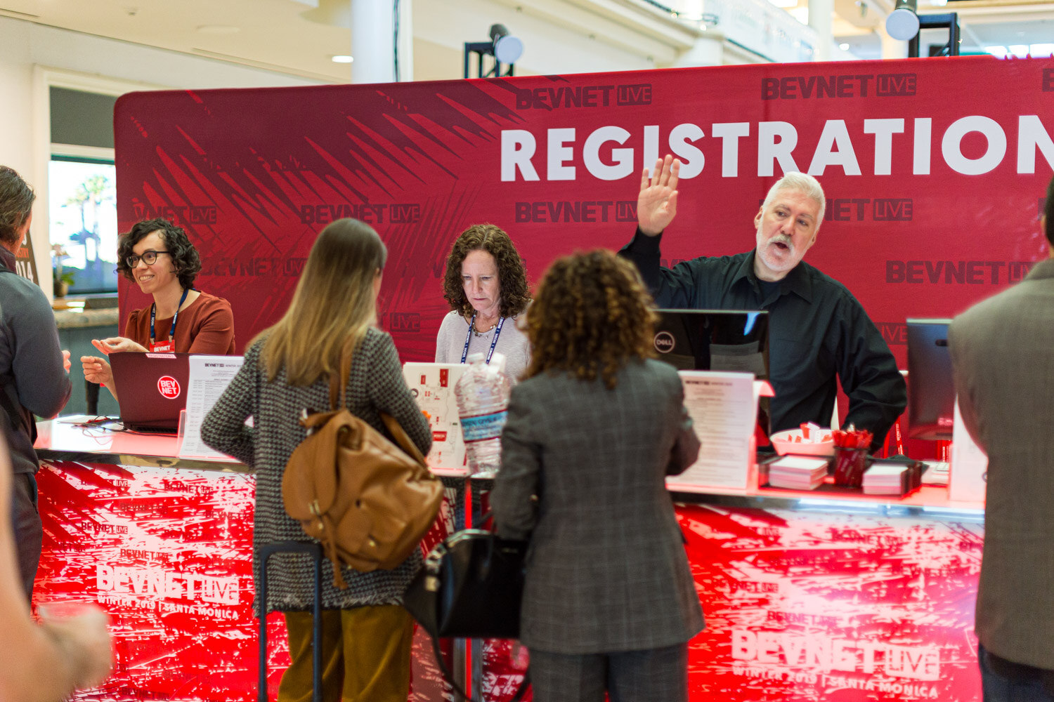 Attendees line up at a red desk under a large Registration sign while staff check them in.