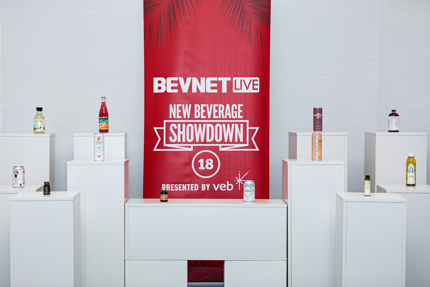 White pedestals display bottles and cans around a red banner reading BevNET Live New Beverage Showdown 18 presented by veb.