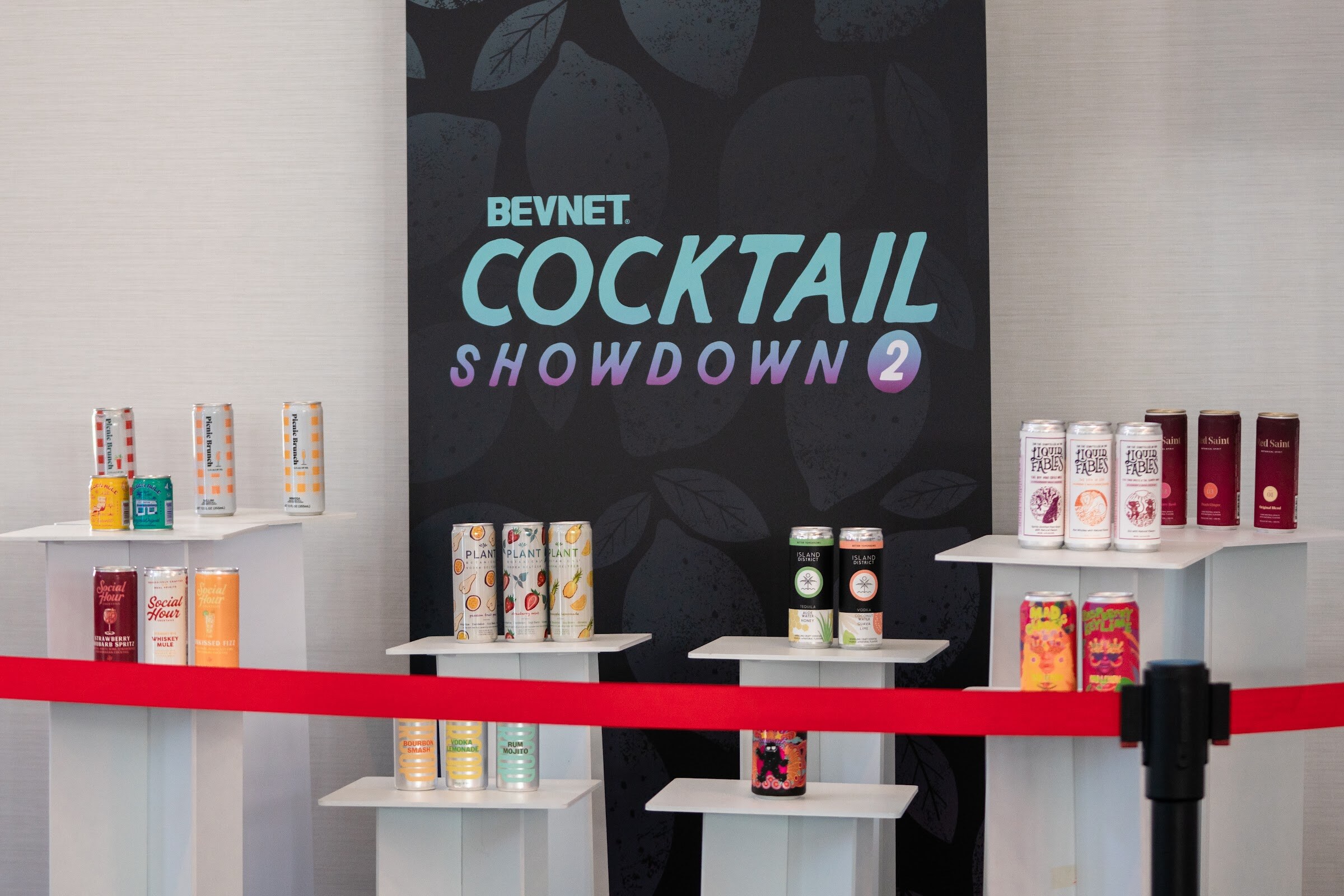 White risers holding rows of canned cocktails behind a red rope in front of a dark sign reading BevNET Cocktail Showdown 2.