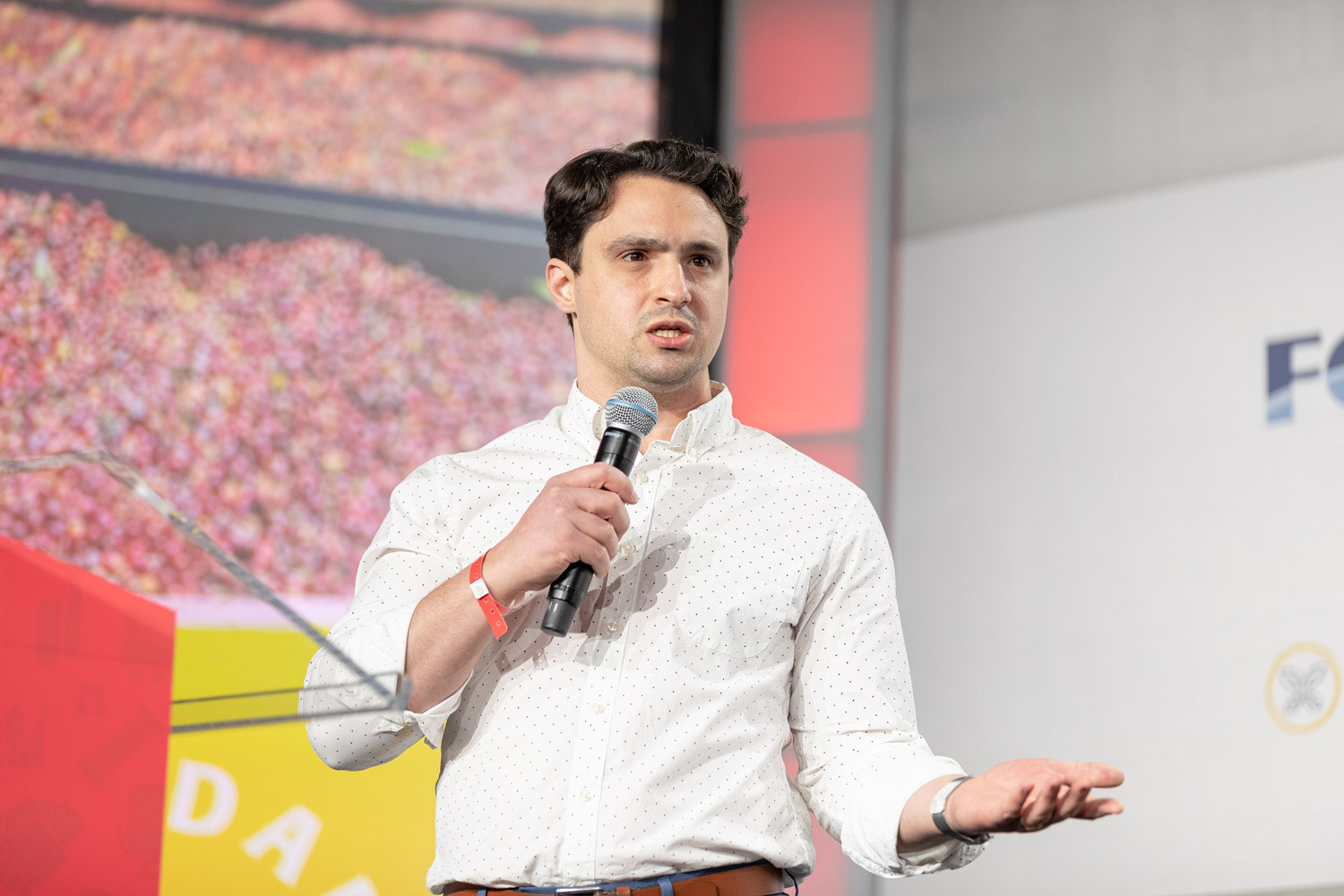 A man in a white dotted shirt holds a microphone and extends one hand in front of a slide of red cranberries.
