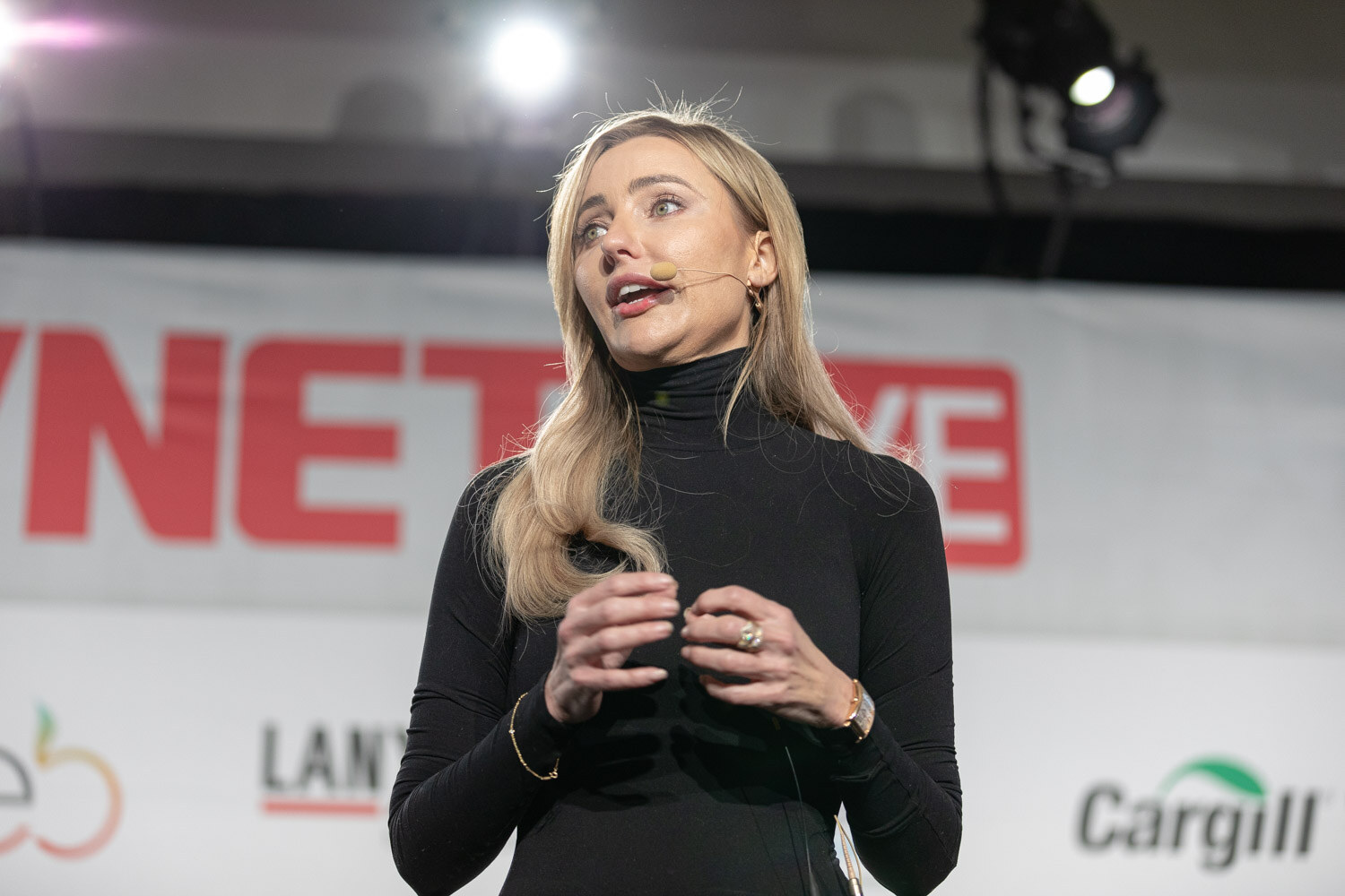 A blonde woman in a black turtleneck speaks with her hands together in front of a BevNET Live banner with Cargill and Lanxess logos behind her.
