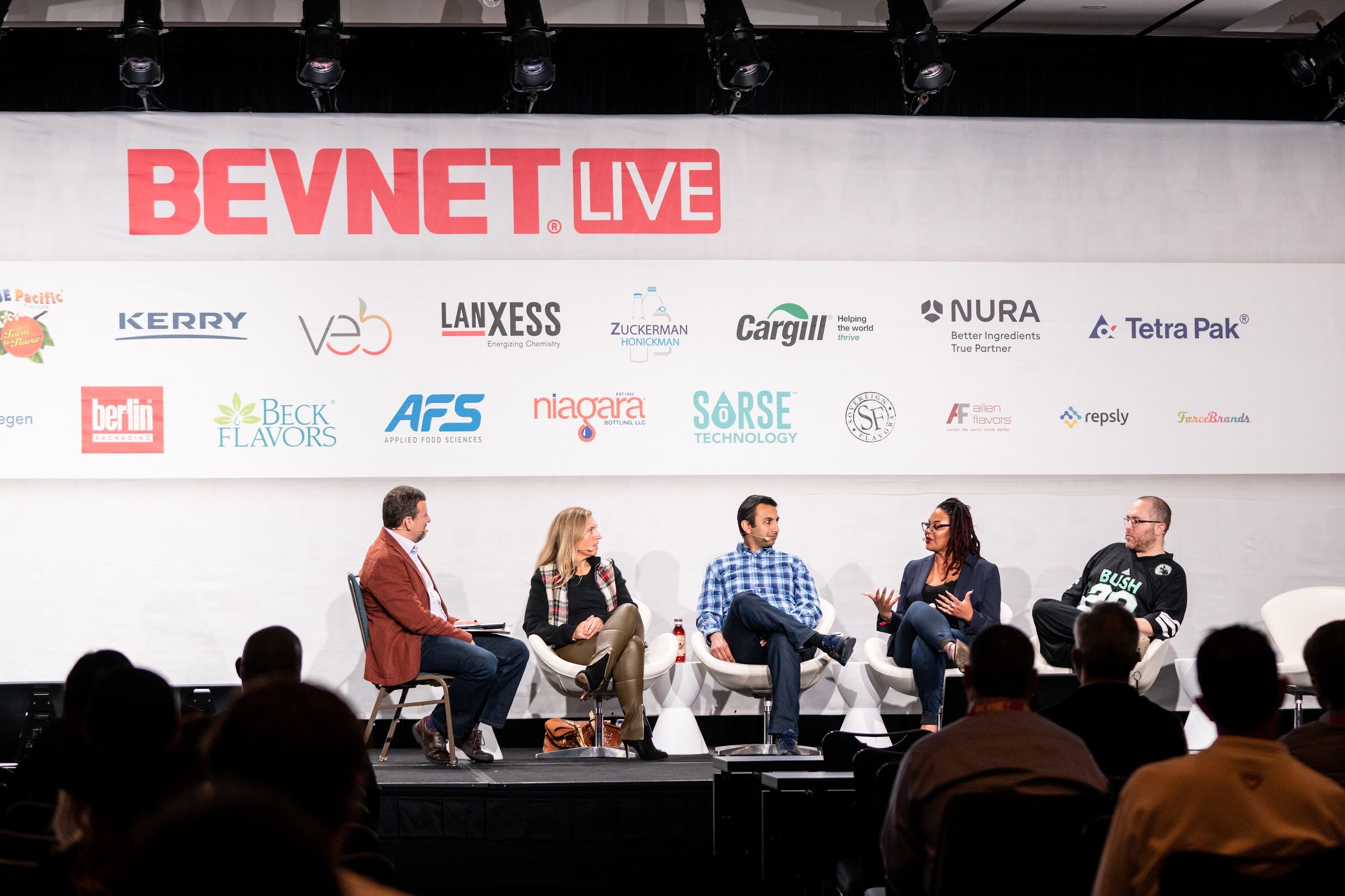Five people seated on a stage under a BevNET Live banner and sponsor logos, with audience members' heads in the foreground.