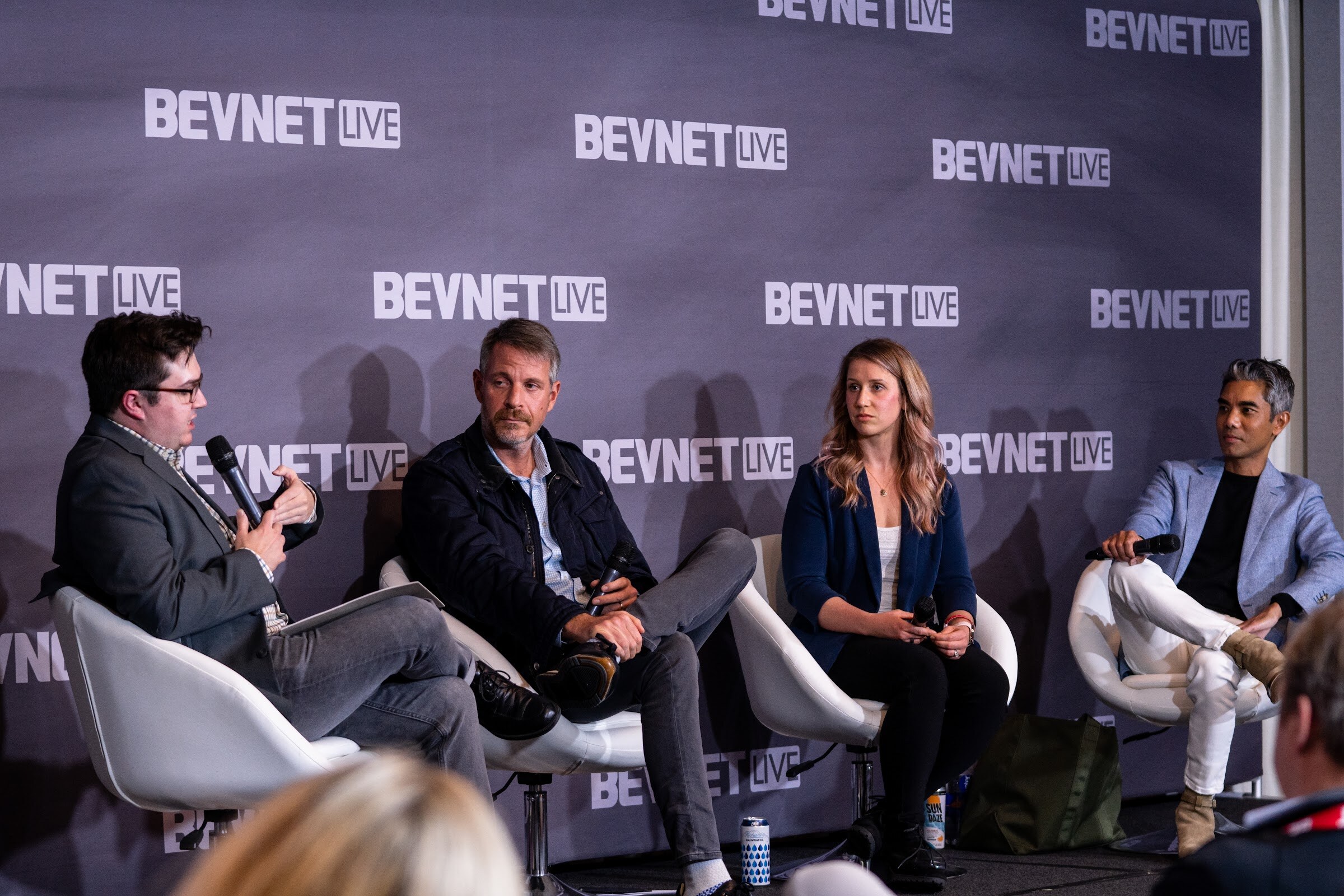 Four people seated in white chairs in front of a purple BevNET Live wall, with the moderator at left holding a microphone.