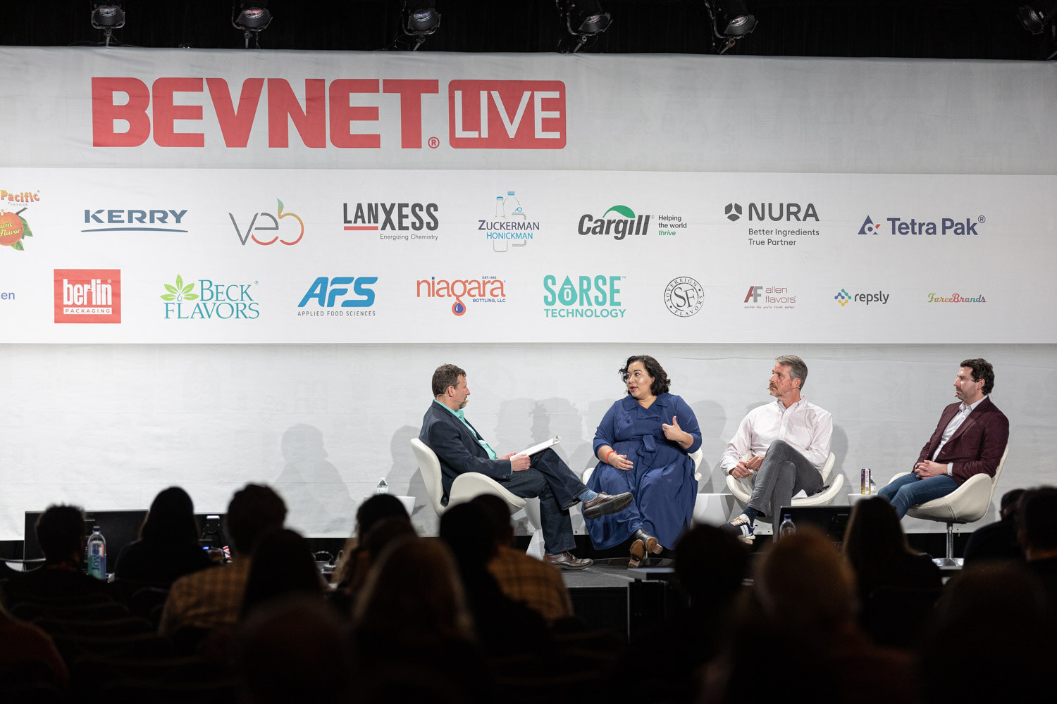 A wide view of four people seated on a stage under a BevNET Live banner and sponsor logos, with audience heads in the foreground.