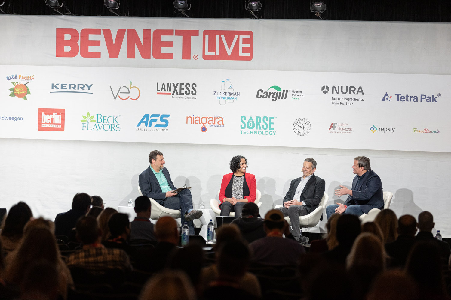 A wide view of four people seated on stage under the BevNET Live banner with sponsor logos and audience members in the foreground.