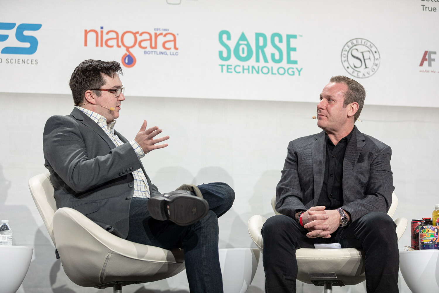 Two men in blazers sit in white chairs in front of a sponsor wall with Niagara and Sorse Technology logos, one gesturing as he speaks.