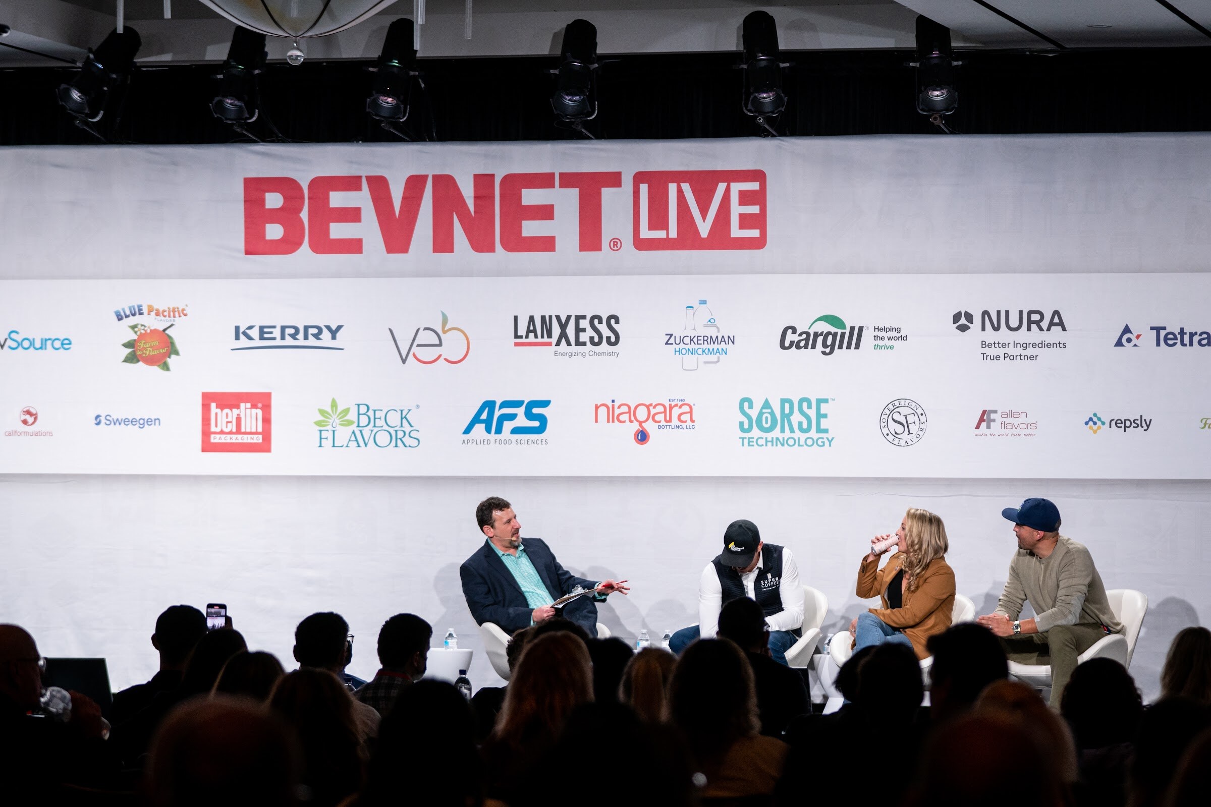 Four people seated on stage under a BevNET Live banner with sponsor logos, with audience members seated in front.