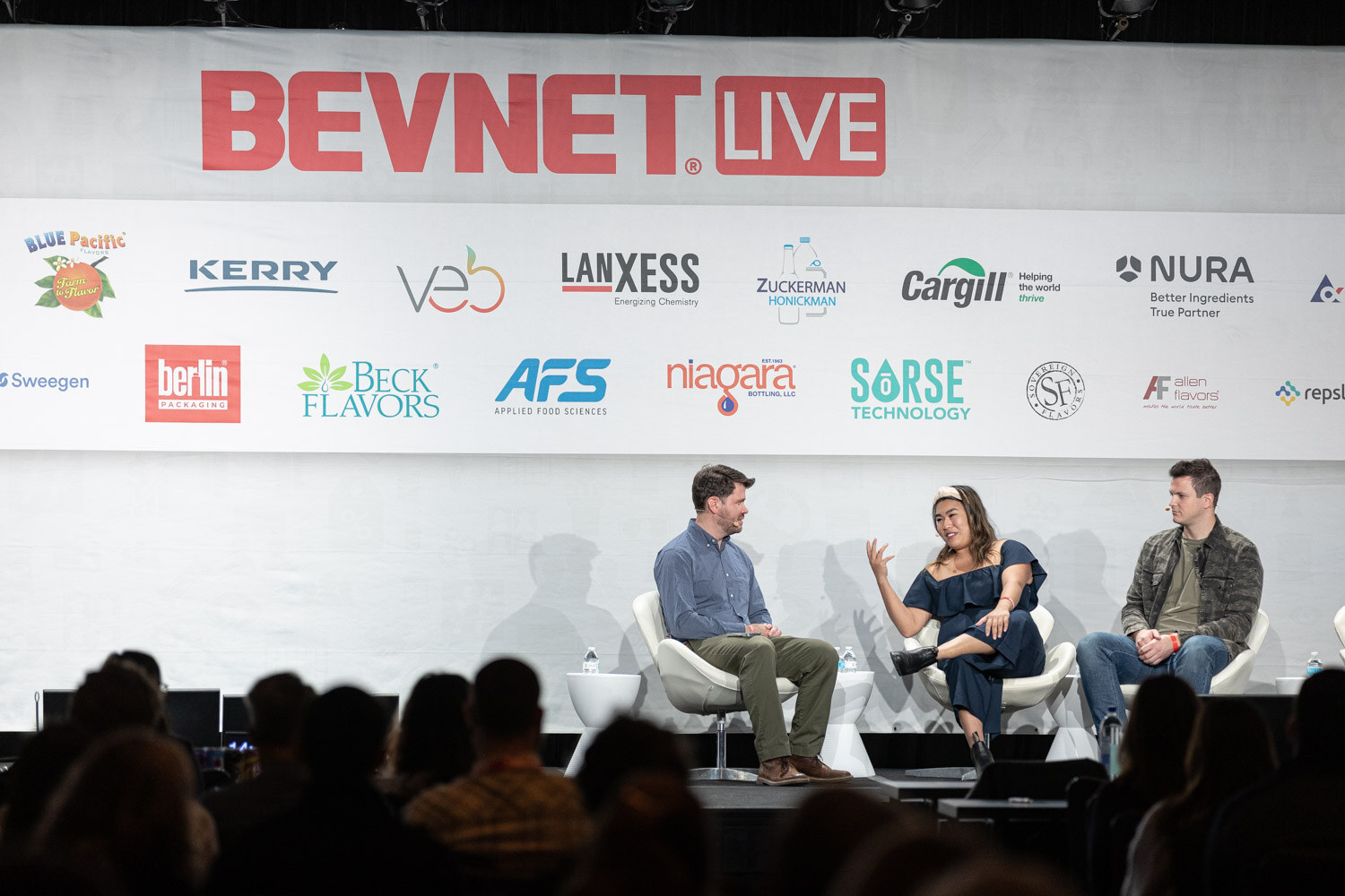 A wide view of three people seated on a stage under a BevNET Live banner and sponsor logos, with the audience's heads in the foreground.