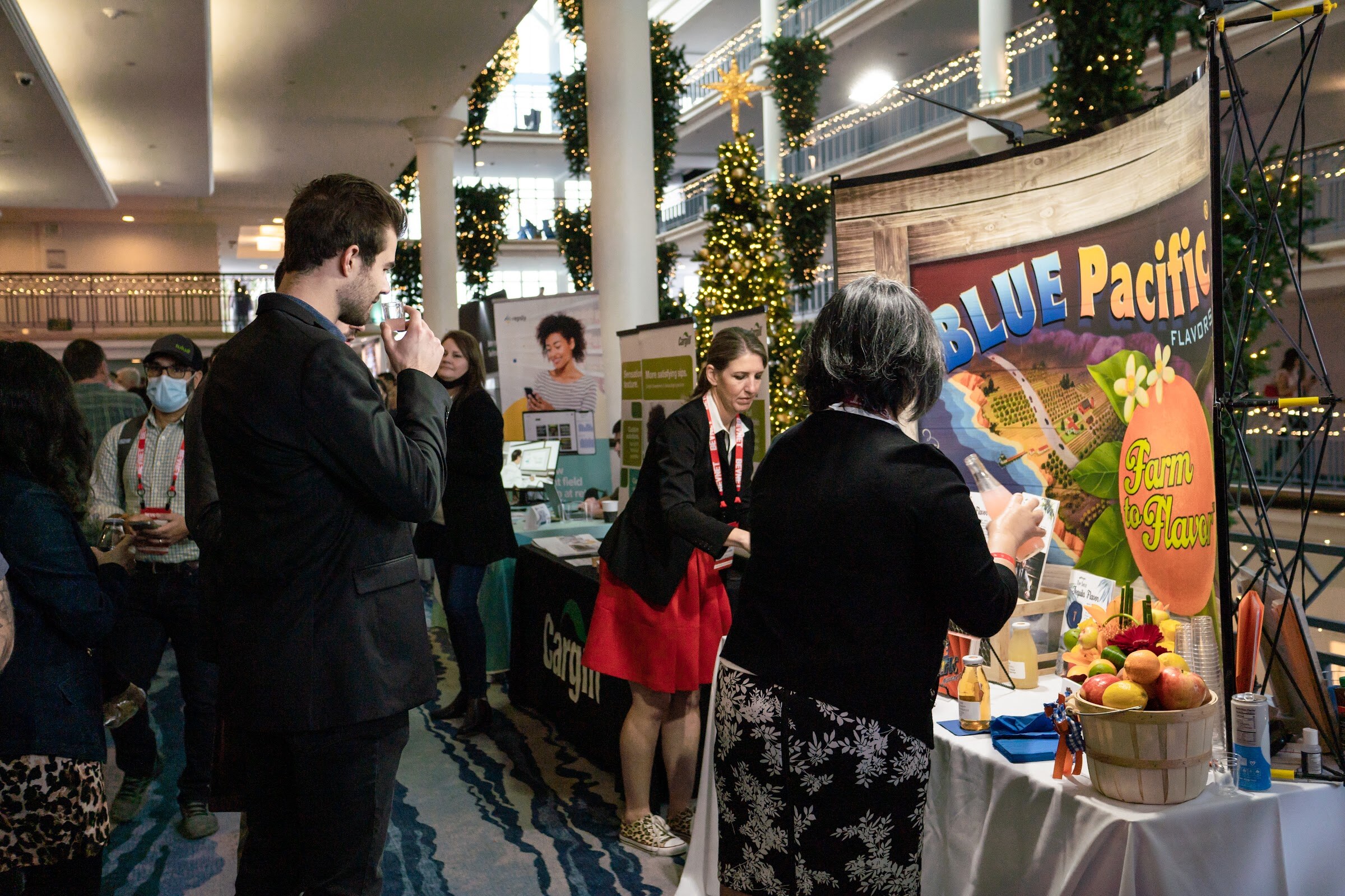 Several people stand in front of a curved Blue Pacific Flavors backdrop with a fruit basket on the table, with Christmas decorations in the background.