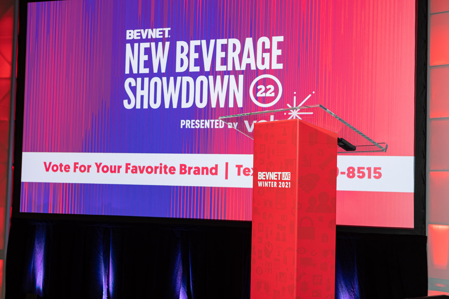 A large screen reading BevNET New Beverage Showdown 22 presented by veb with the text Vote For Your Favorite Brand, with a red BevNET Live podium in front.