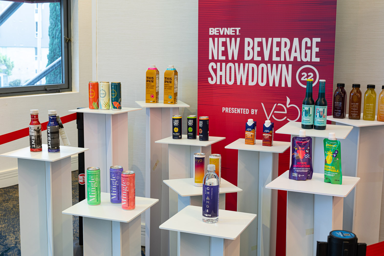 White risers hold cans, bottles and pouches in front of a red banner reading BevNET New Beverage Showdown 22 presented by veb.