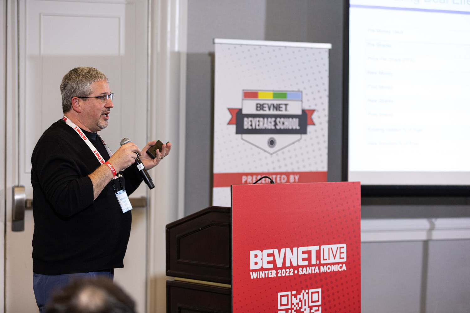 A man in glasses and a black sweater with a BevNET lanyard stands beside a red podium that reads BevNET Live Winter 2022 Santa Monica.