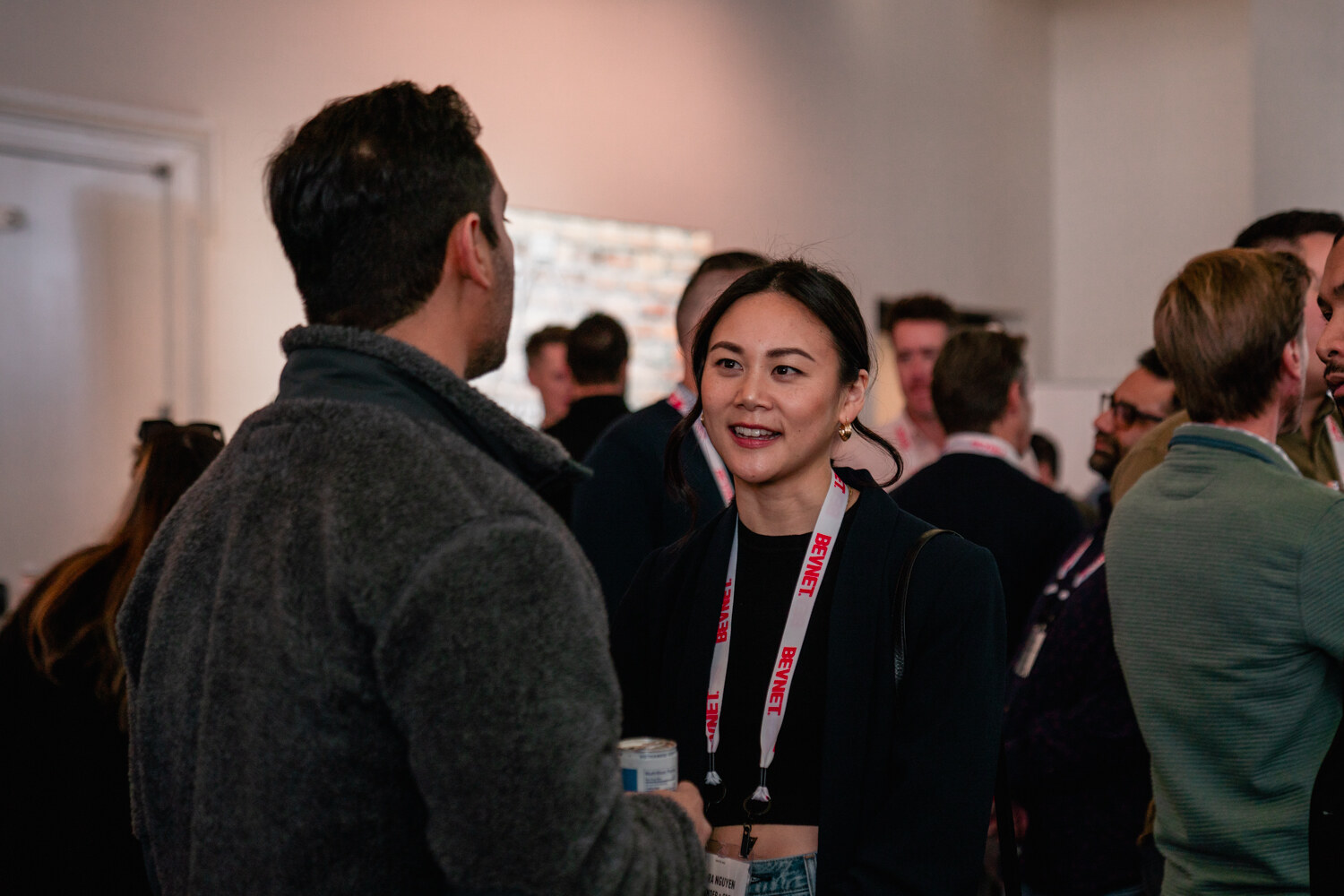 A woman with a BevNET lanyard smiles as she talks with a man in a gray fleece with his back to the camera.