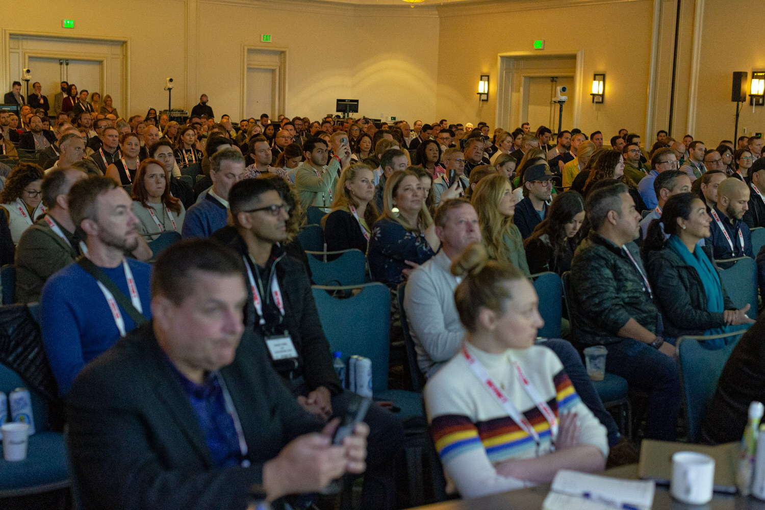 A crowded ballroom of attendees seated in rows with BevNET lanyards, many looking at the stage, with sconces on the walls behind them.