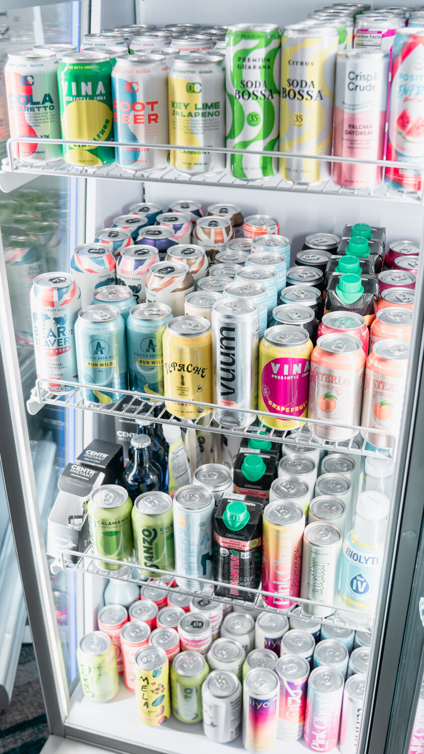 A glass-door cooler filled with rows of canned drinks, including cans reading Vuum and Soda Mossa.