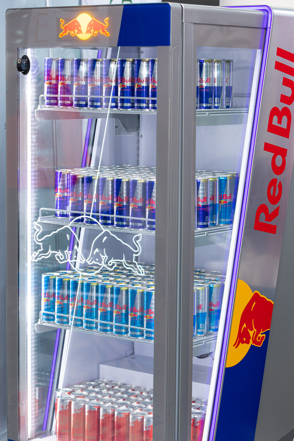 A glass-door Red Bull cooler holding several shelves of silver and blue Red Bull cans.