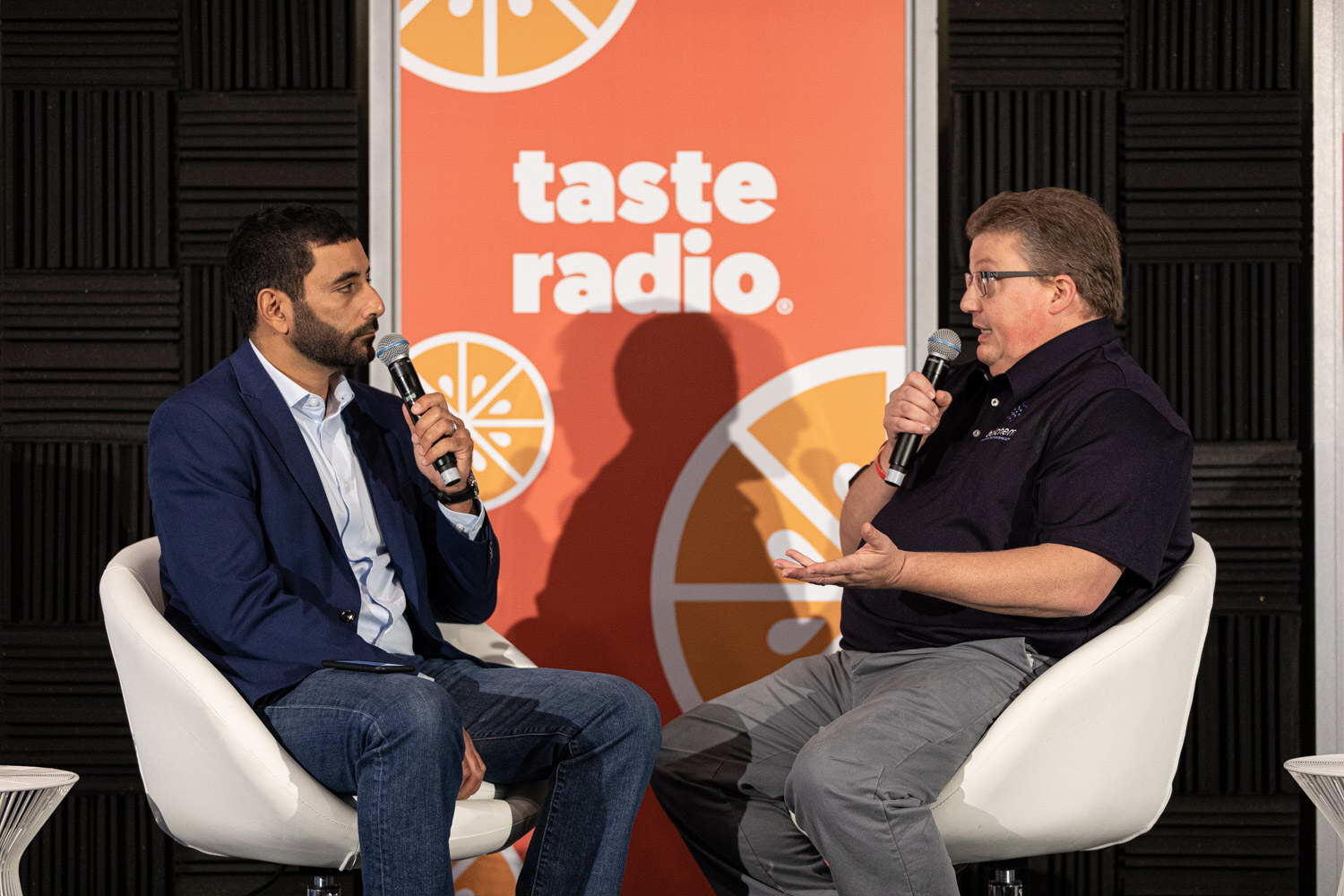 Two men in white chairs hold microphones and talk in front of a Taste Radio banner, with a BevNET Live sign at right.