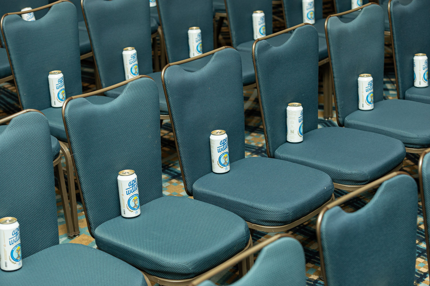 Rows of teal ballroom chairs with a can of ape water standing on each seat.