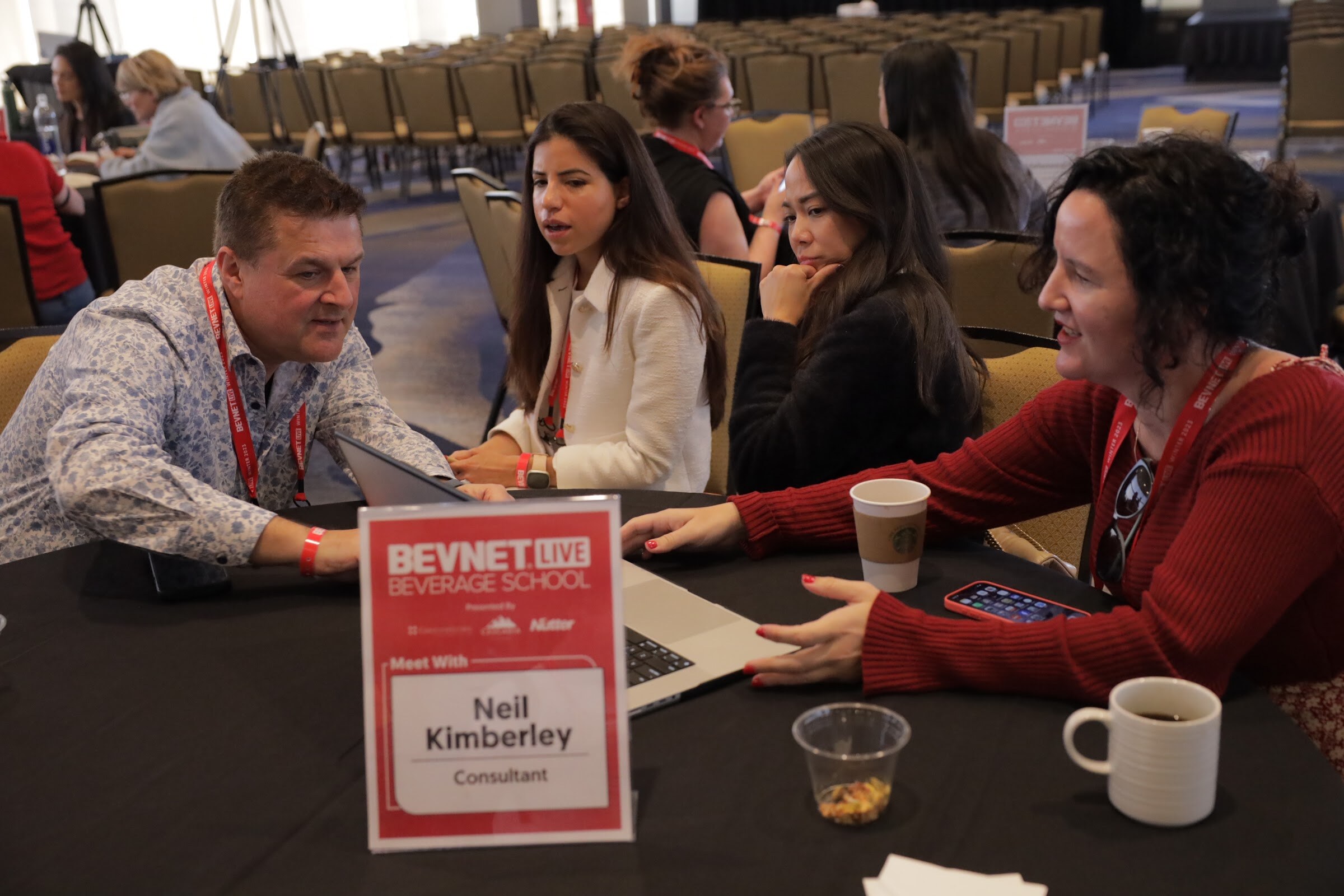Four people sit at a table with a laptop and coffee cup and a Beverage School table sign.